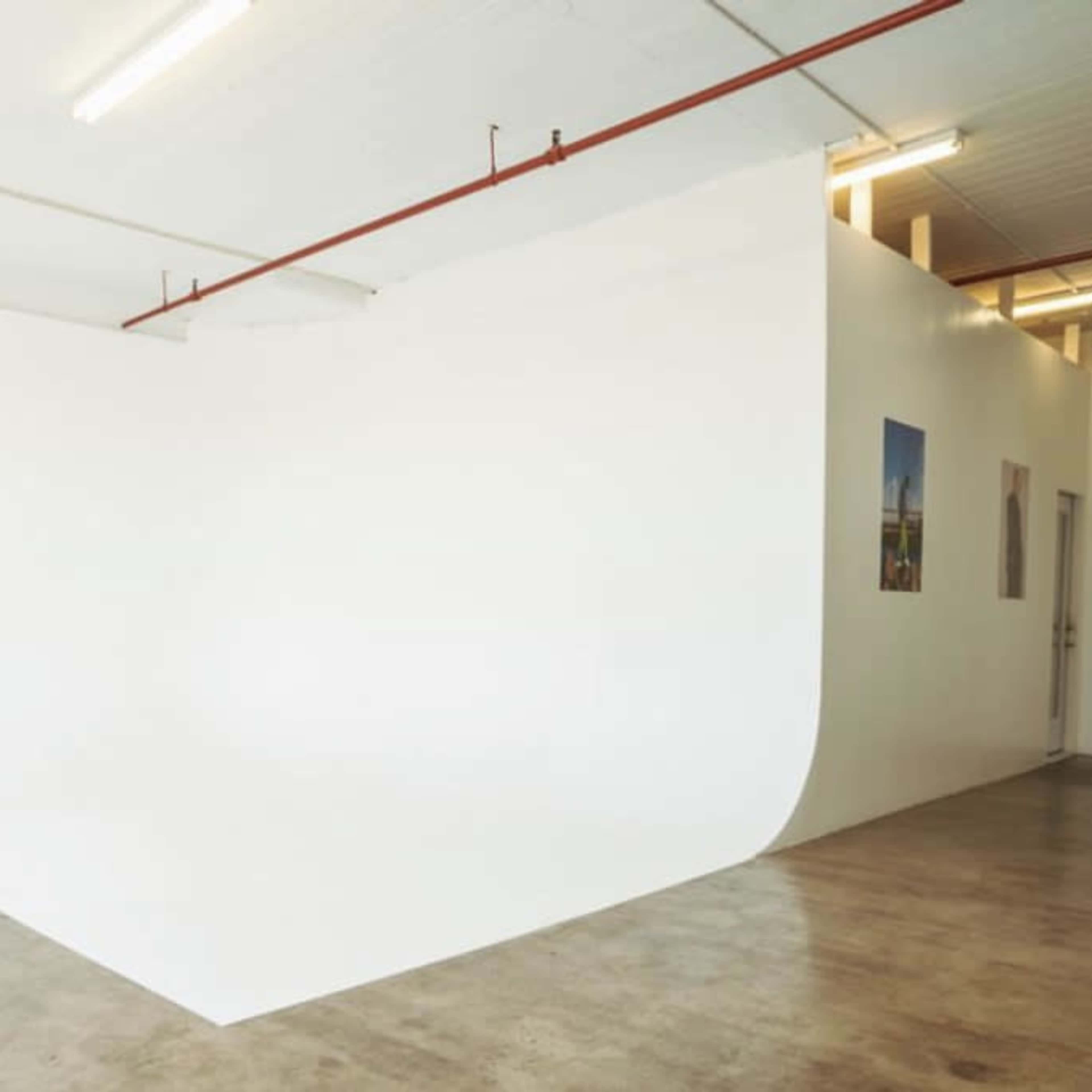 A minimalist interior space featuring a seamless white wall and a gray couch in one corner.