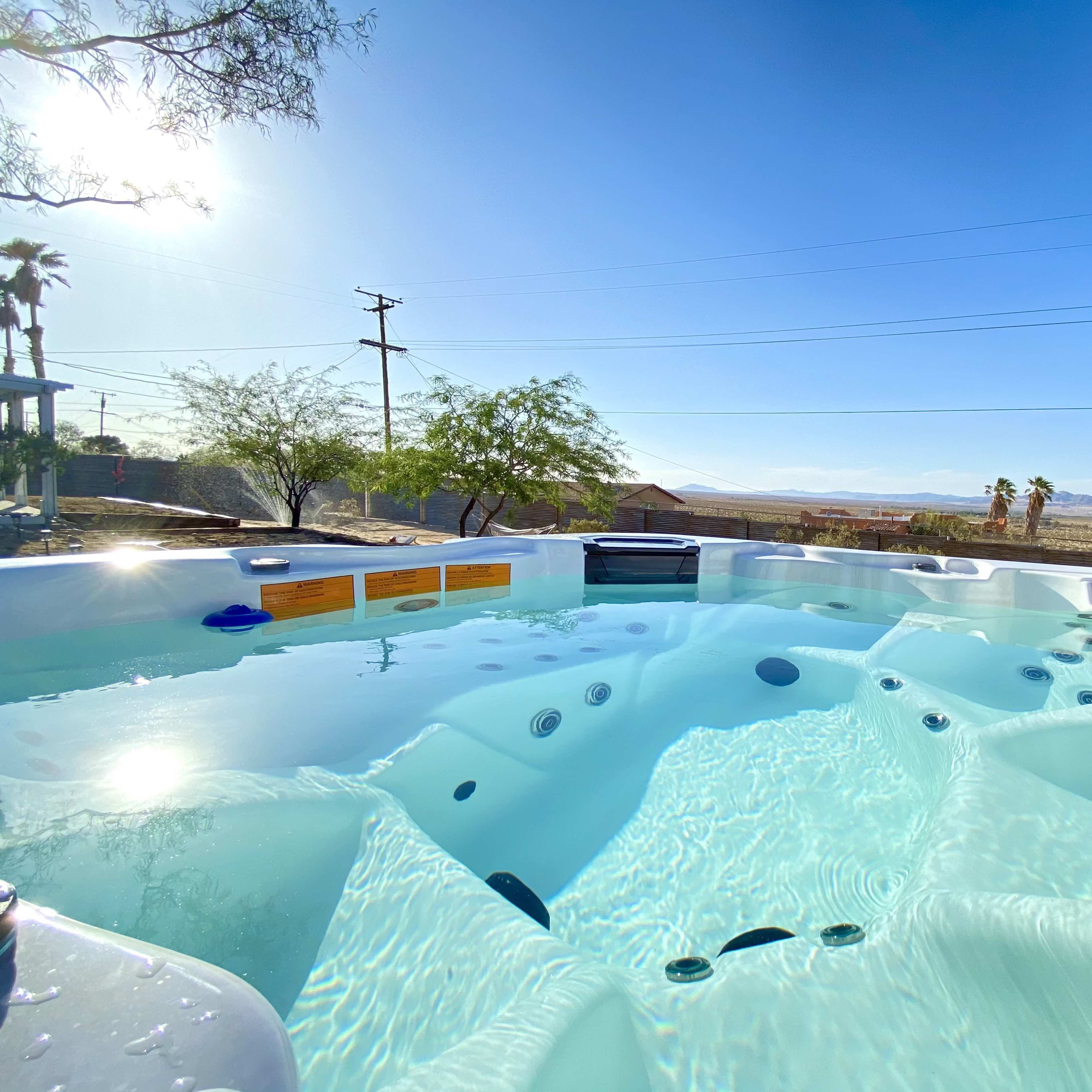 A hot tub filled with clear water is set against a backdrop of a clear sky and distant mountains.