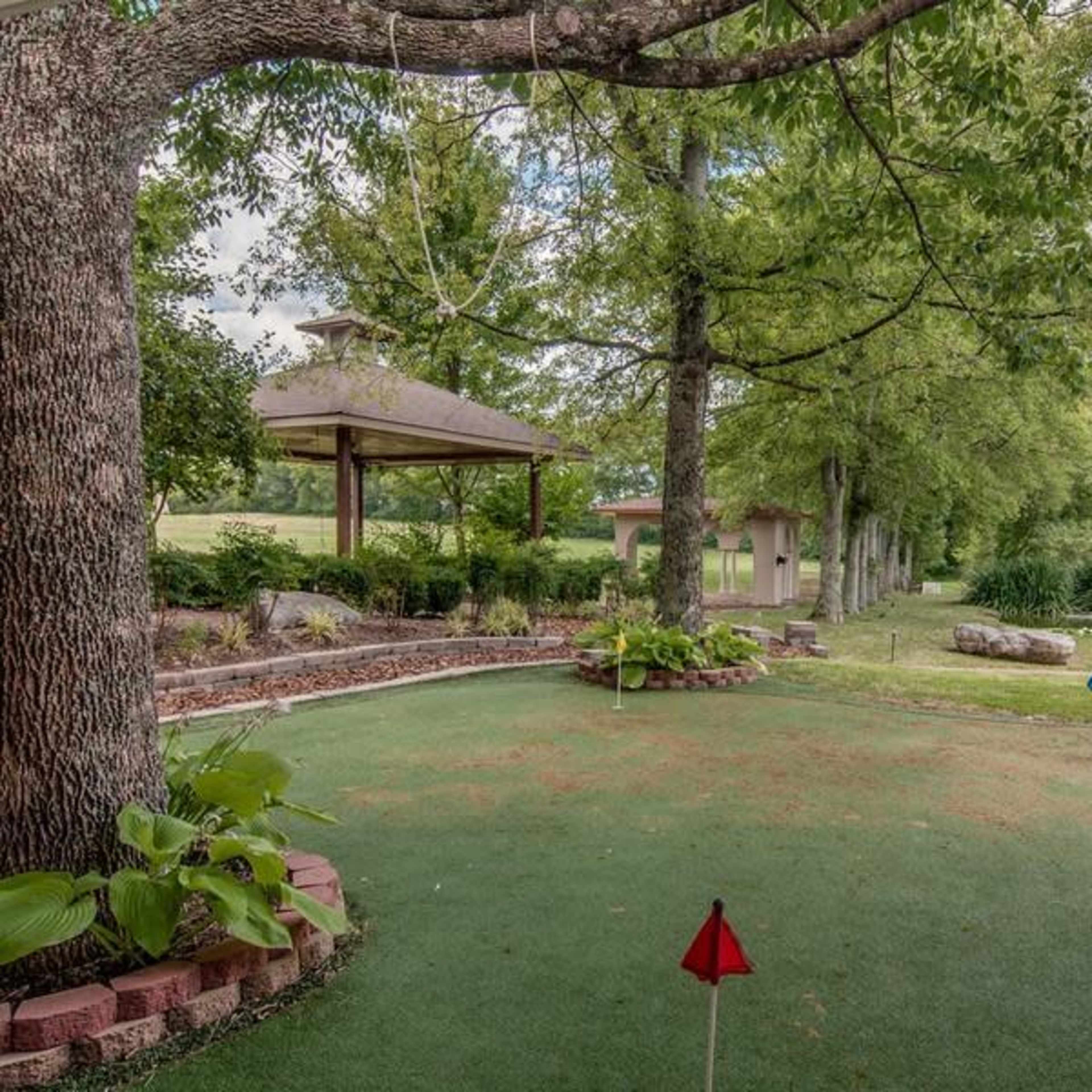 A landscaped backyard with a putting green, a gazebo, and several trees.