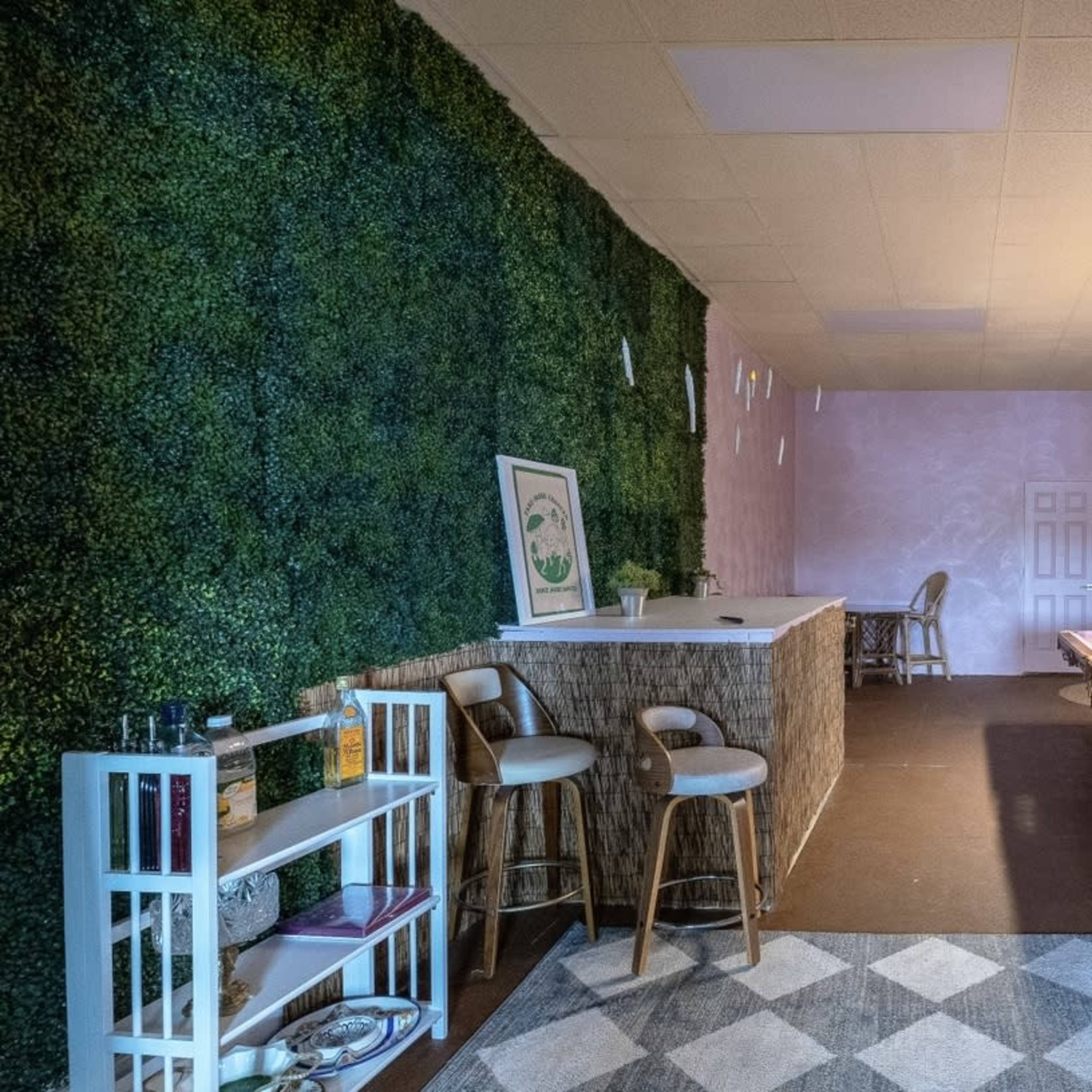 A room with a green wall, a pool table, a bar area with stools, and a patterned carpet.