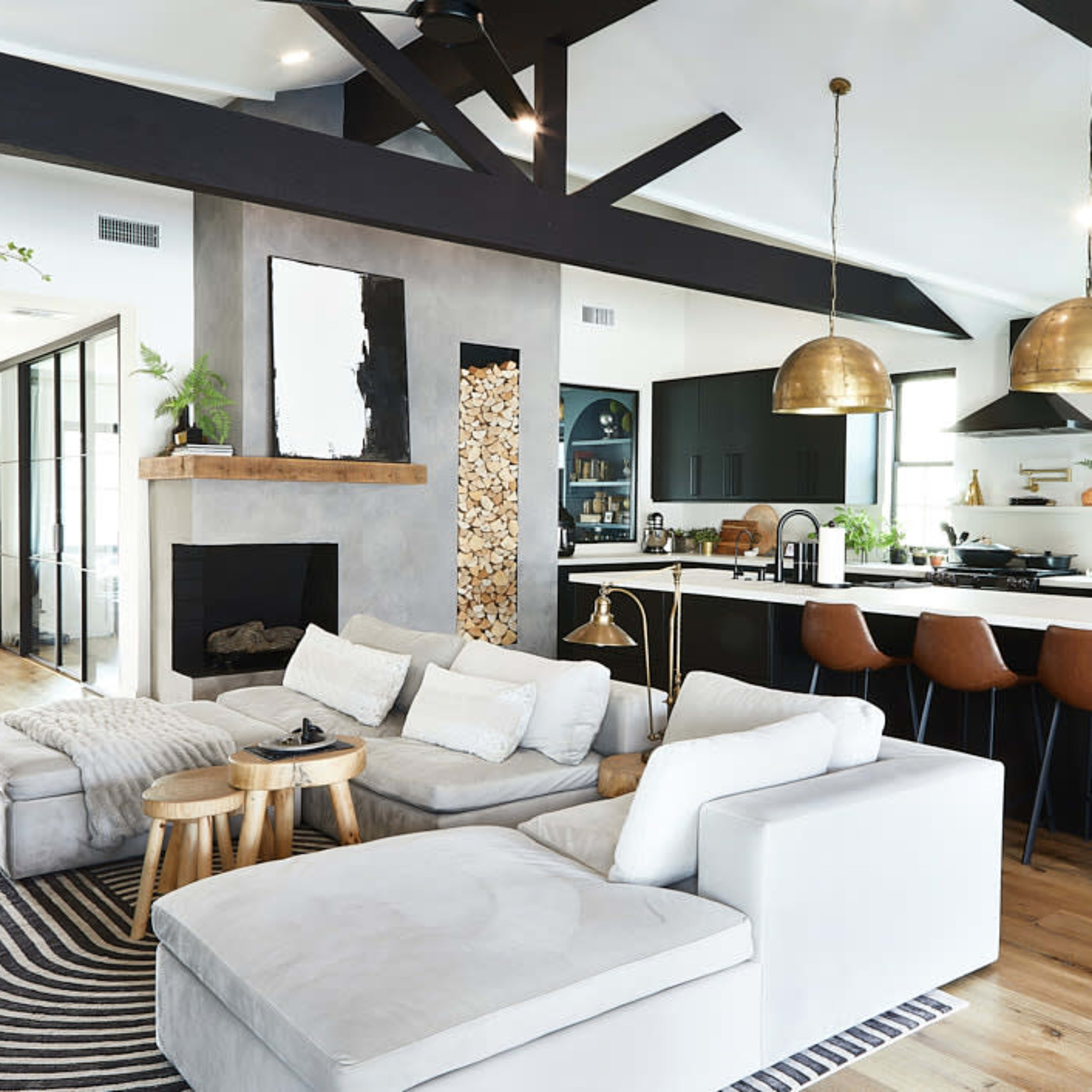 A modern living area featuring a spacious open-concept kitchen and living room with black cabinetry, wooden flooring, and brass pendant lights.