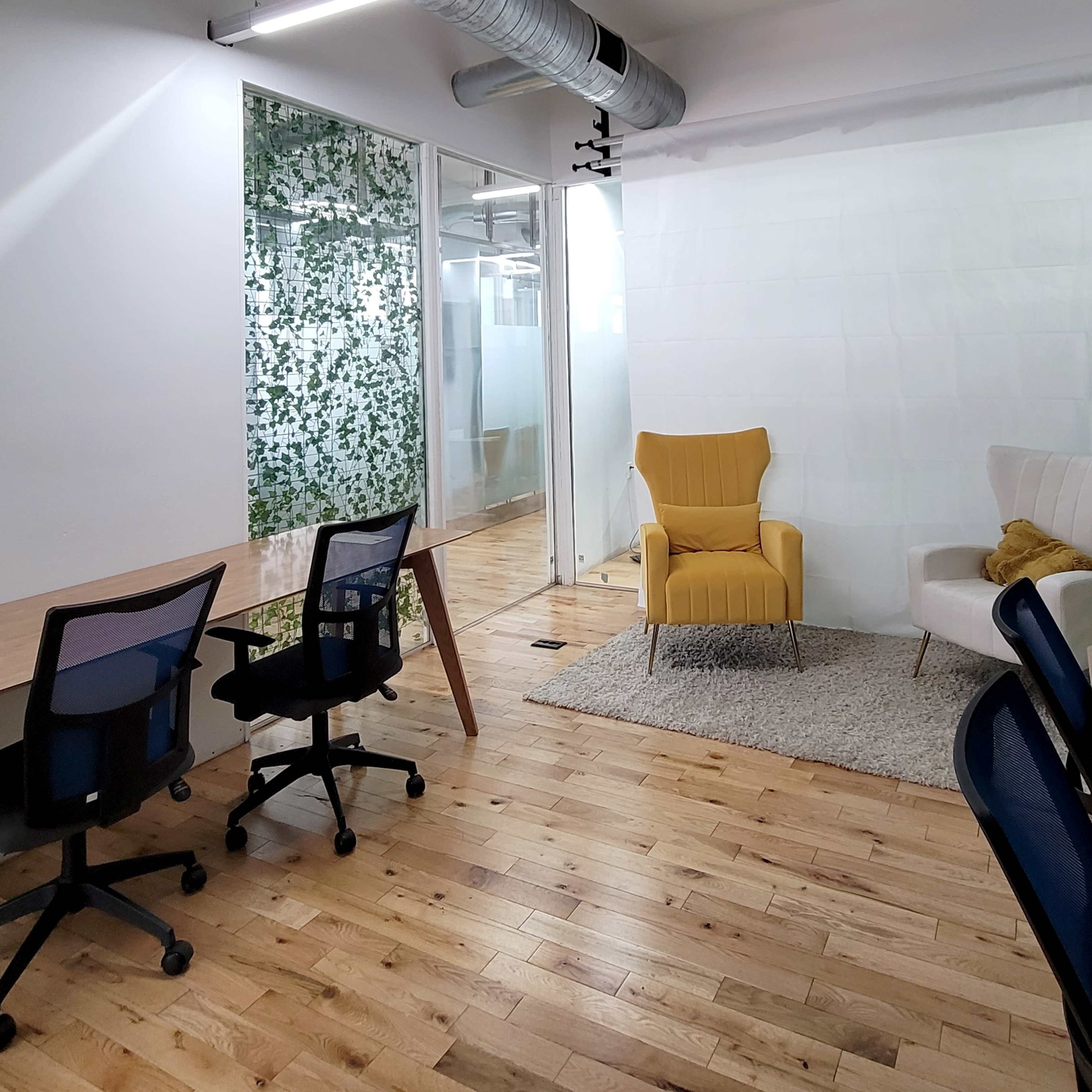 A contemporary office space with two desks, a yellow armchair, a white chair, and greenery on the walls.