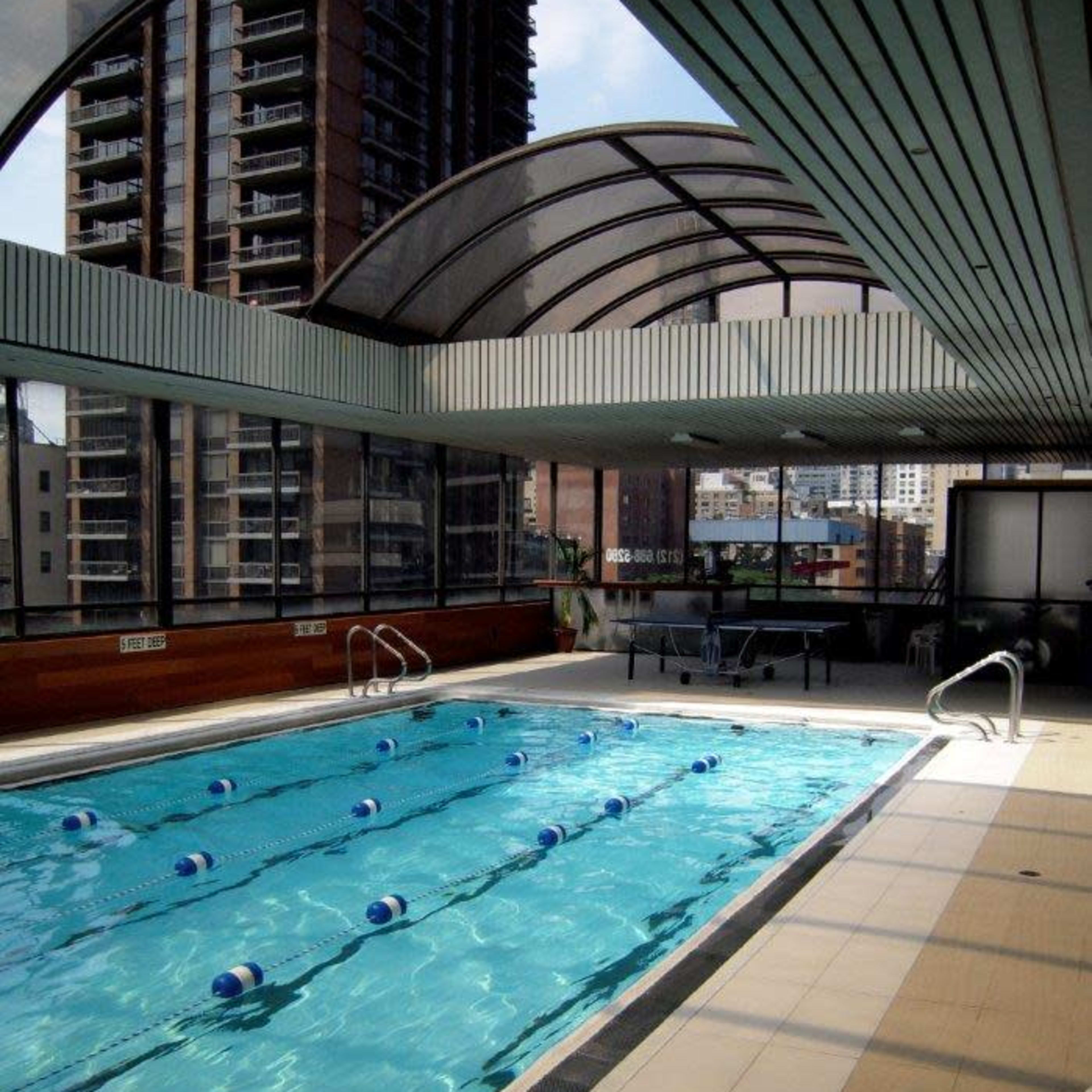 An indoor swimming pool with a glass ceiling, lined with blue lane markers, located in a high-rise building.