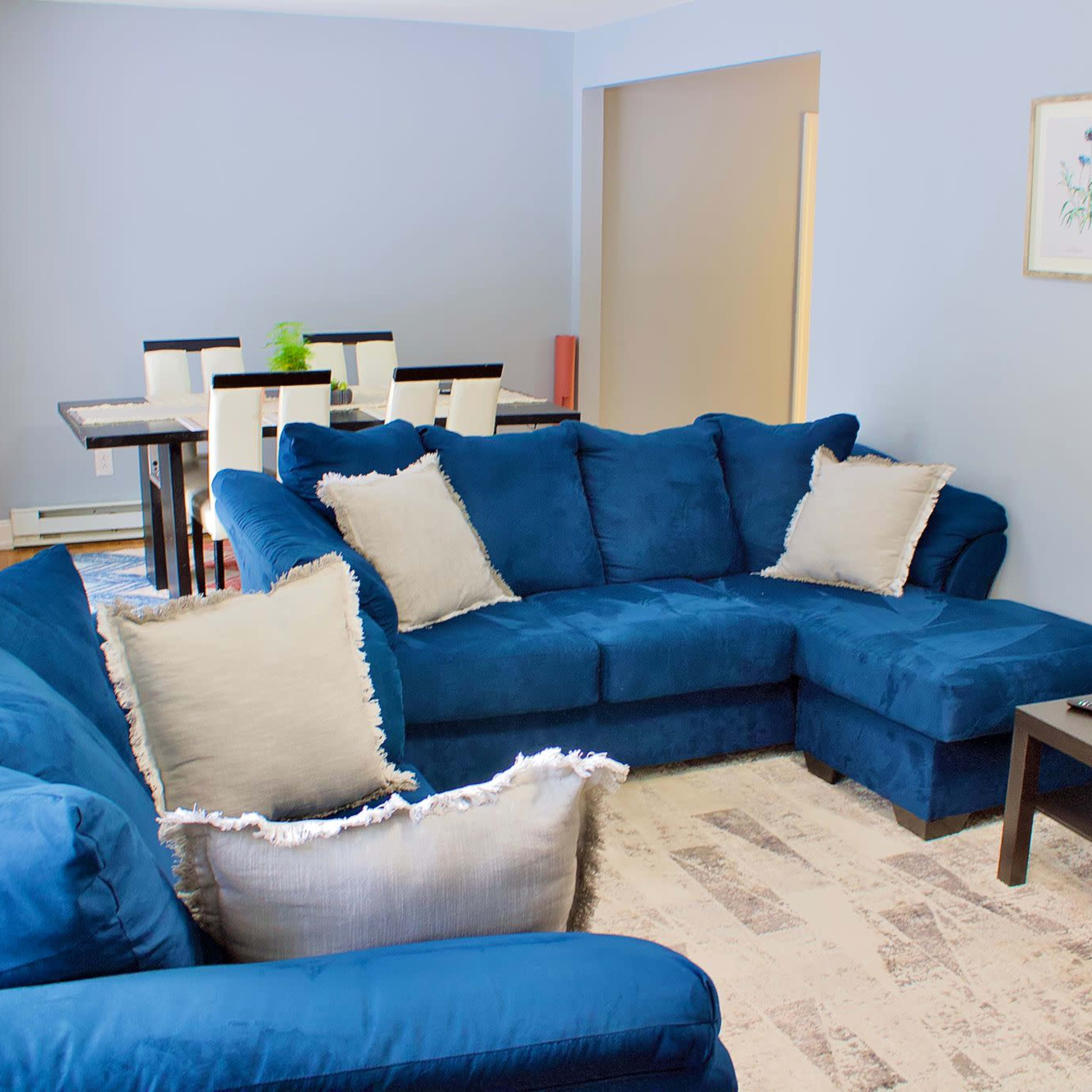A living room featuring a blue sectional sofa, a black coffee table, and a dining area with a table and chairs in the background.