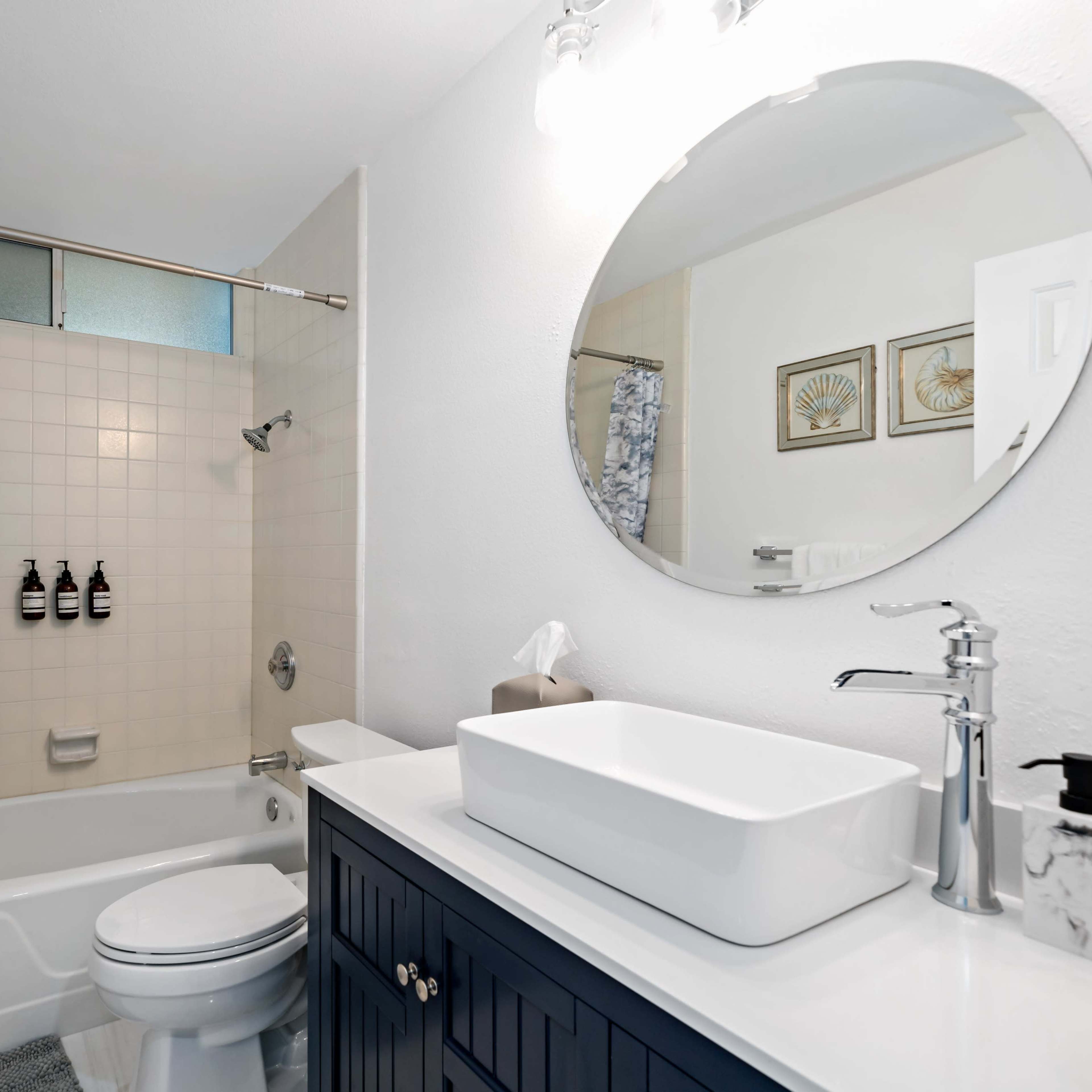 A modern bathroom featuring a bathtub with a shower curtain, a round mirror above a countertop sink, and wall decor.