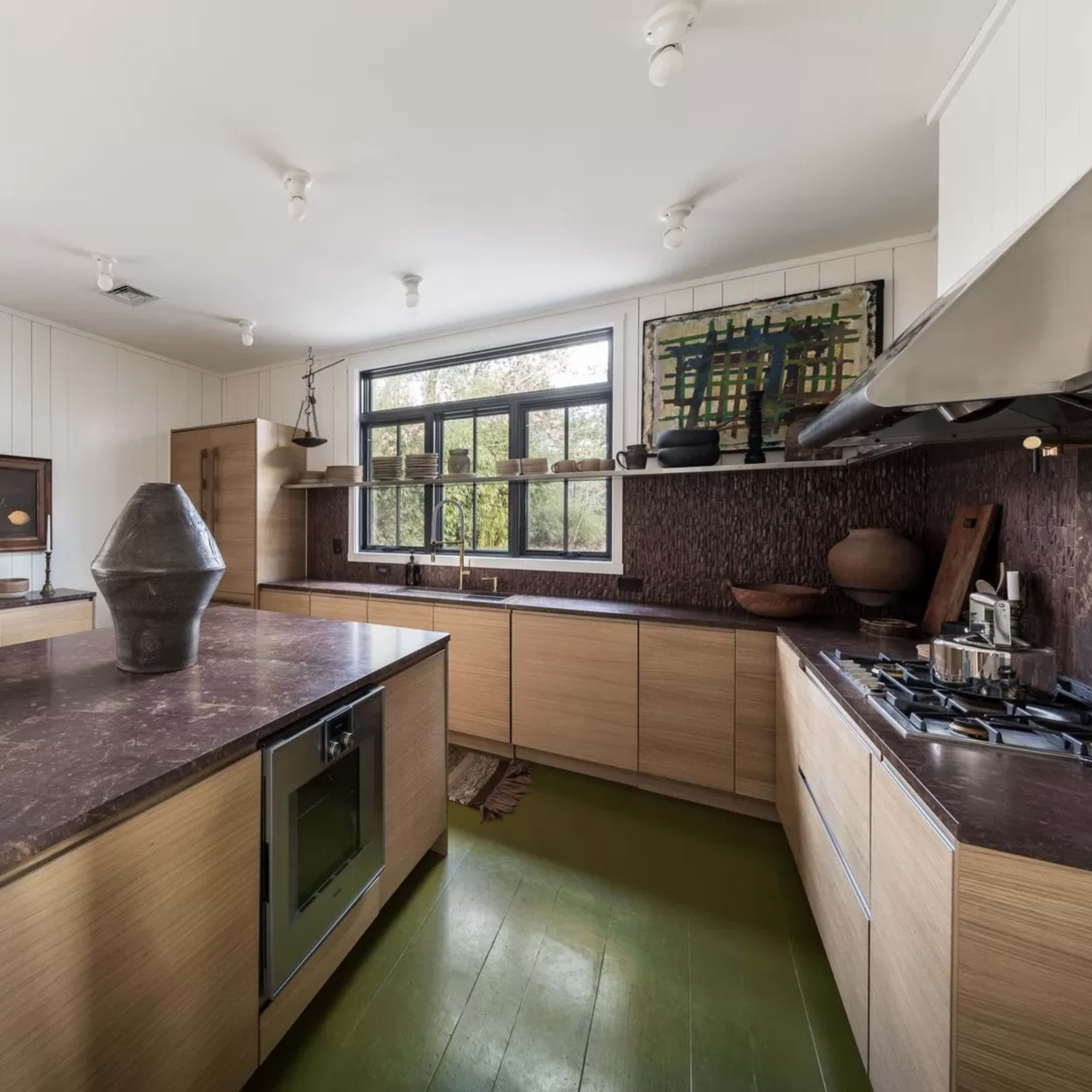 The kitchen features a central island with a dark countertop, wooden cabinetry, and large windows allowing natural light.