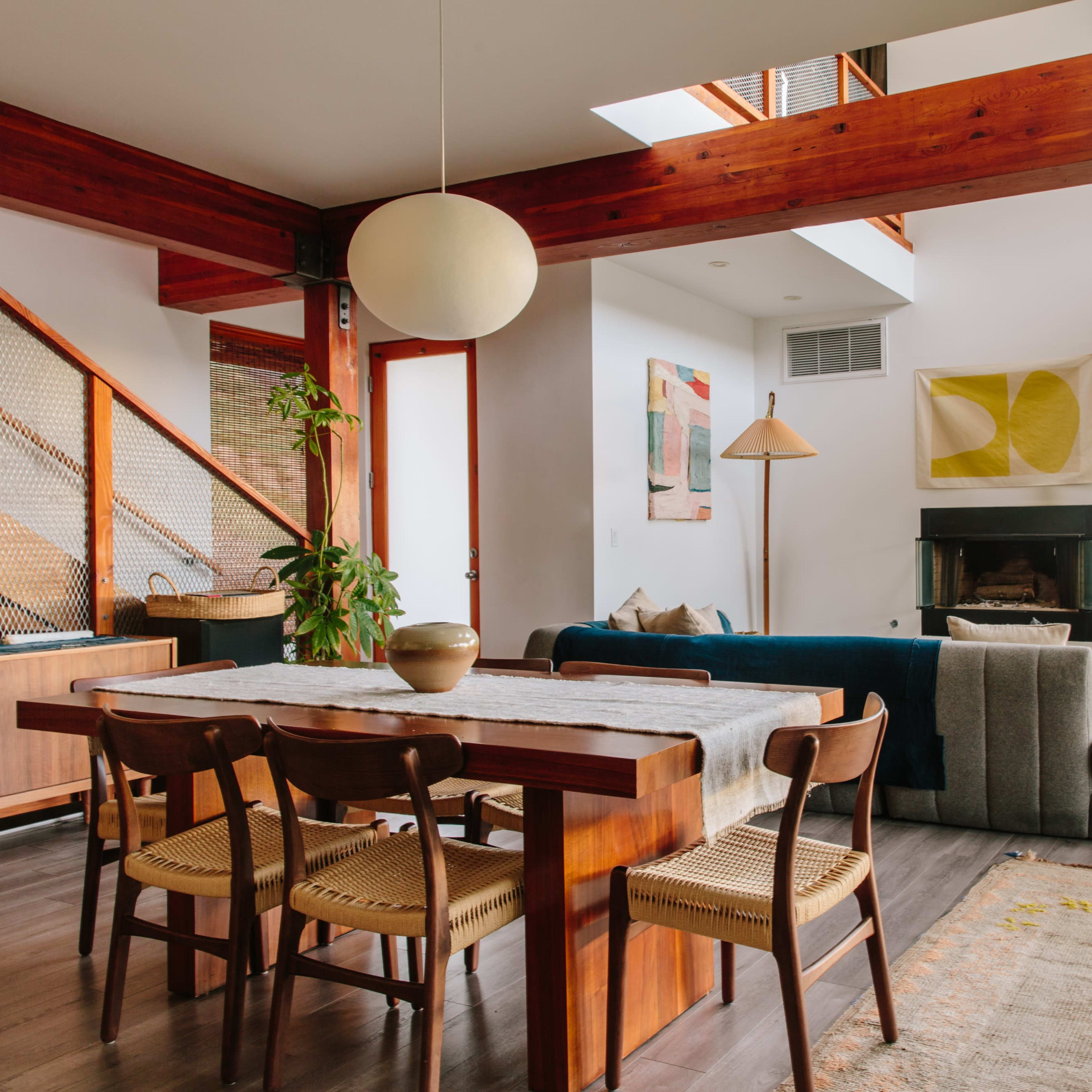 A modern living space with a wooden dining table, a sectional sofa, and large windows that allow natural light to enter.