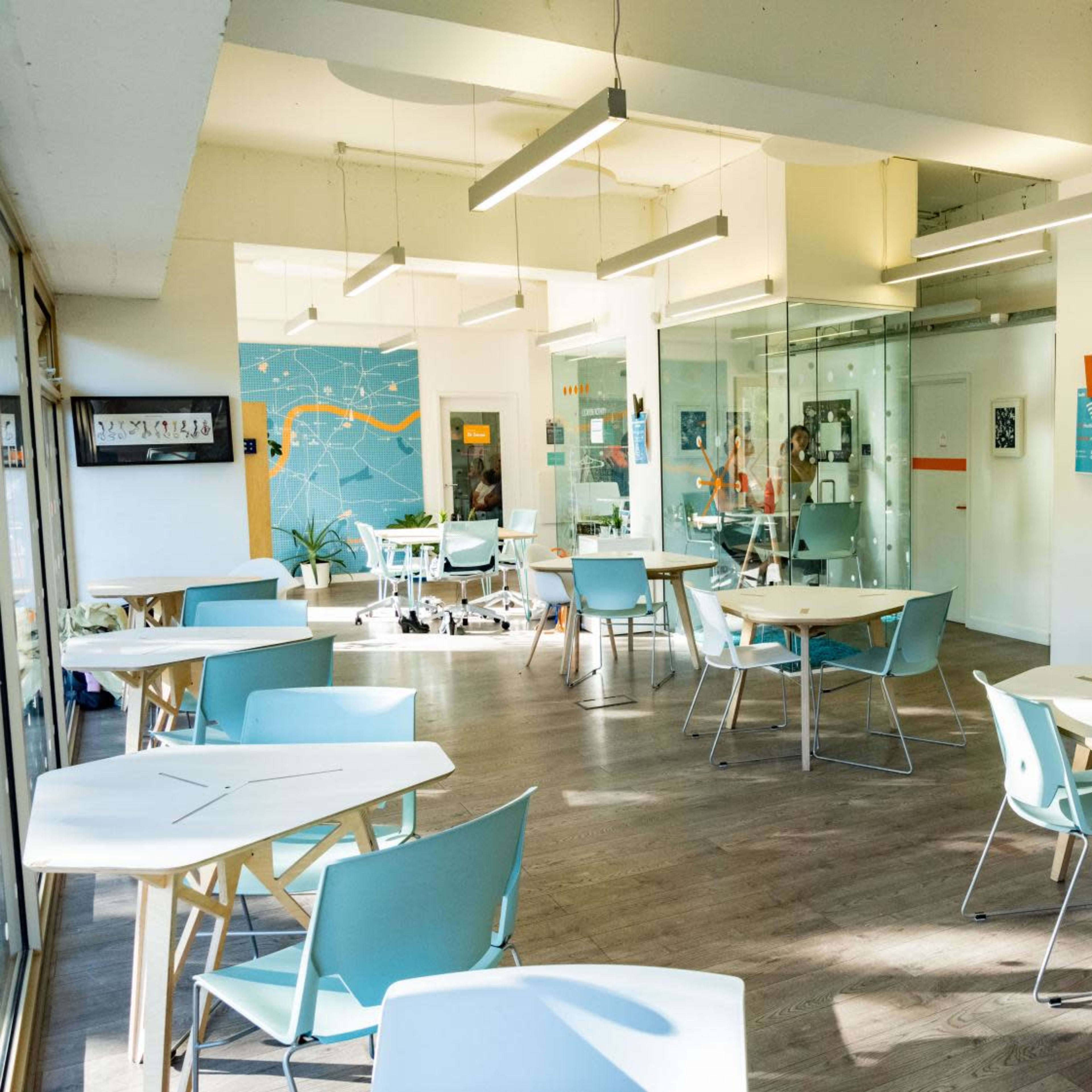 A modern, brightly lit open space with white tables and light blue chairs arranged around the room.