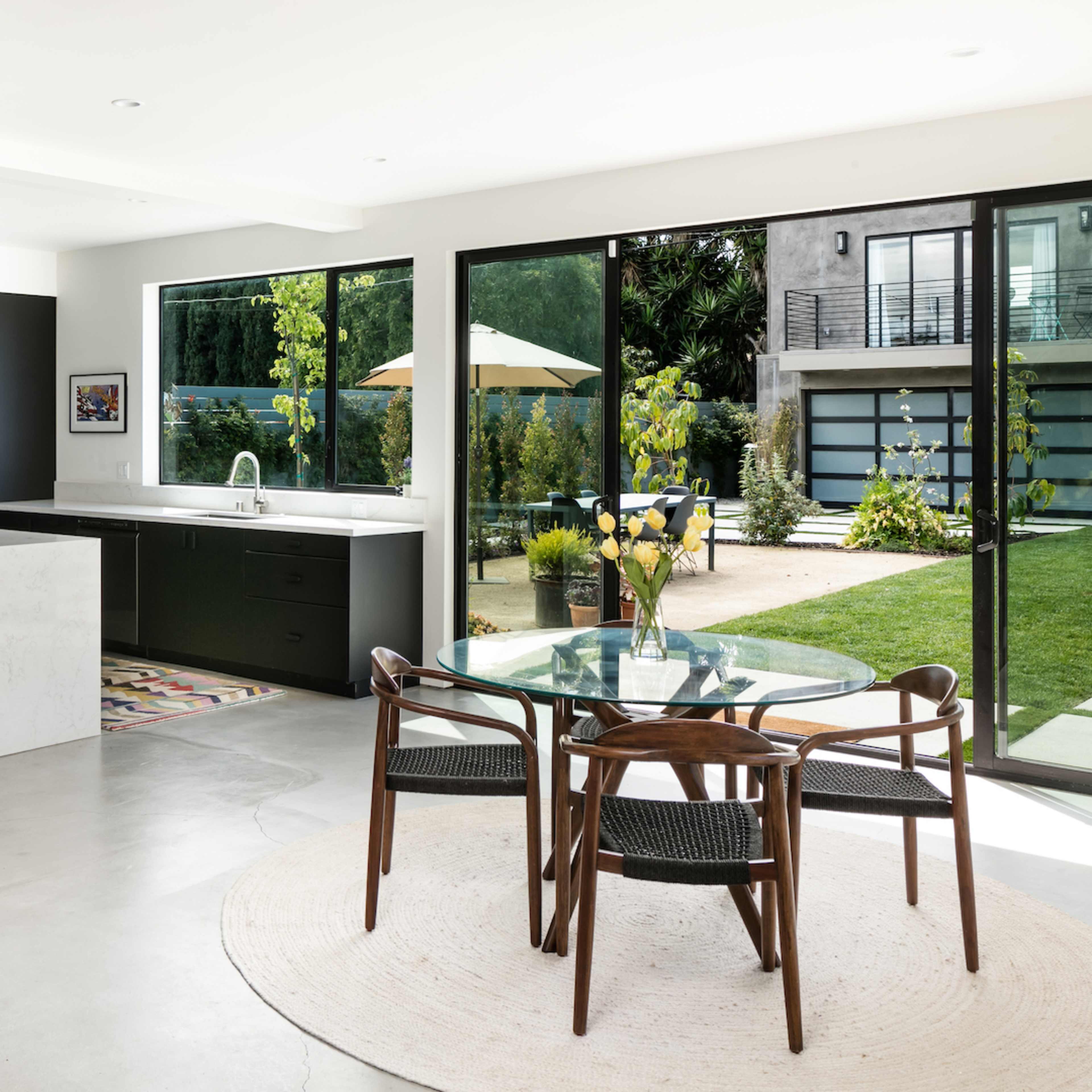 A modern kitchen and dining area with a large island, a round dining table, and glass doors leading to an outdoor space with a lawn and patio.