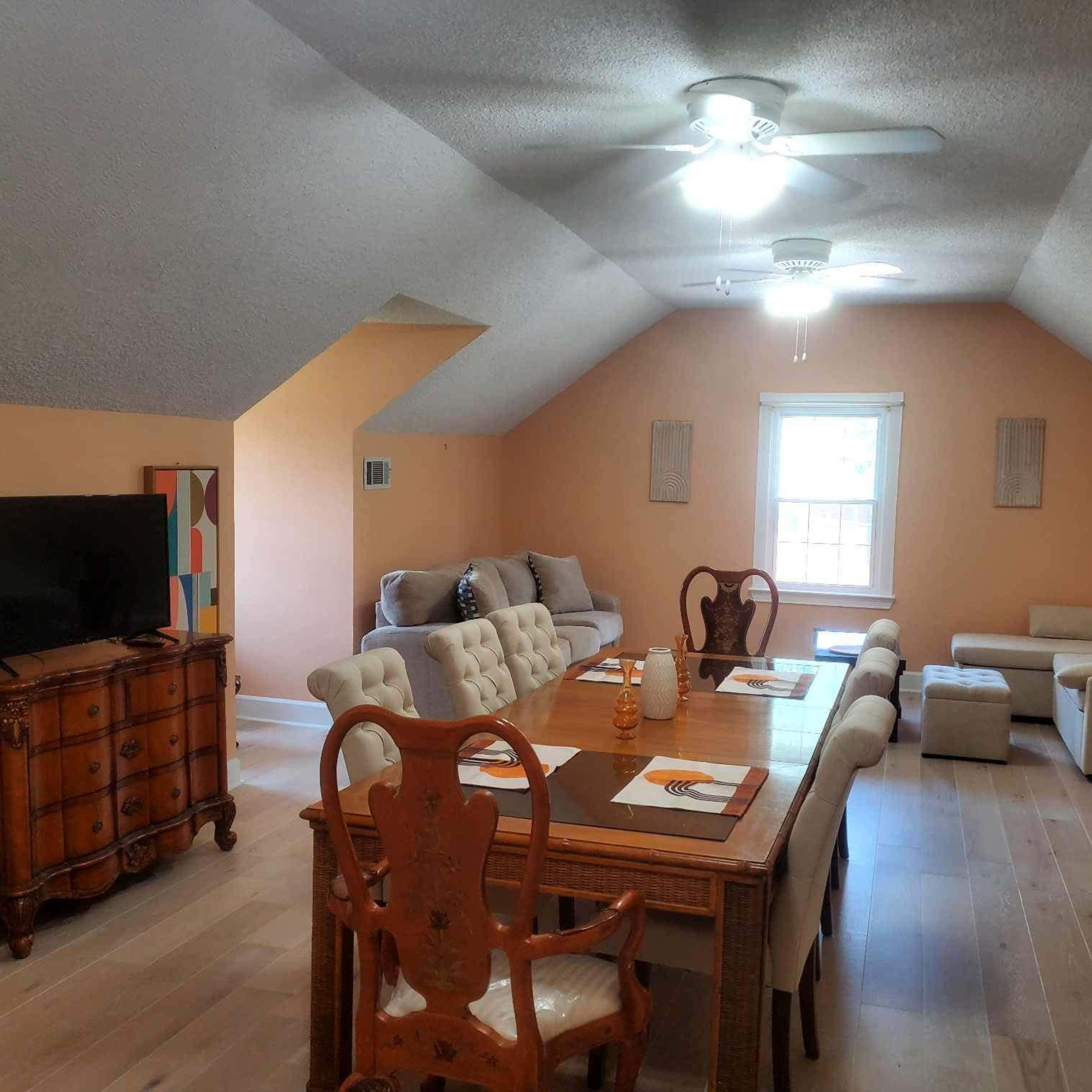 An attic living space furnished with a dining table, chairs, a television, and a seating area with a couch.