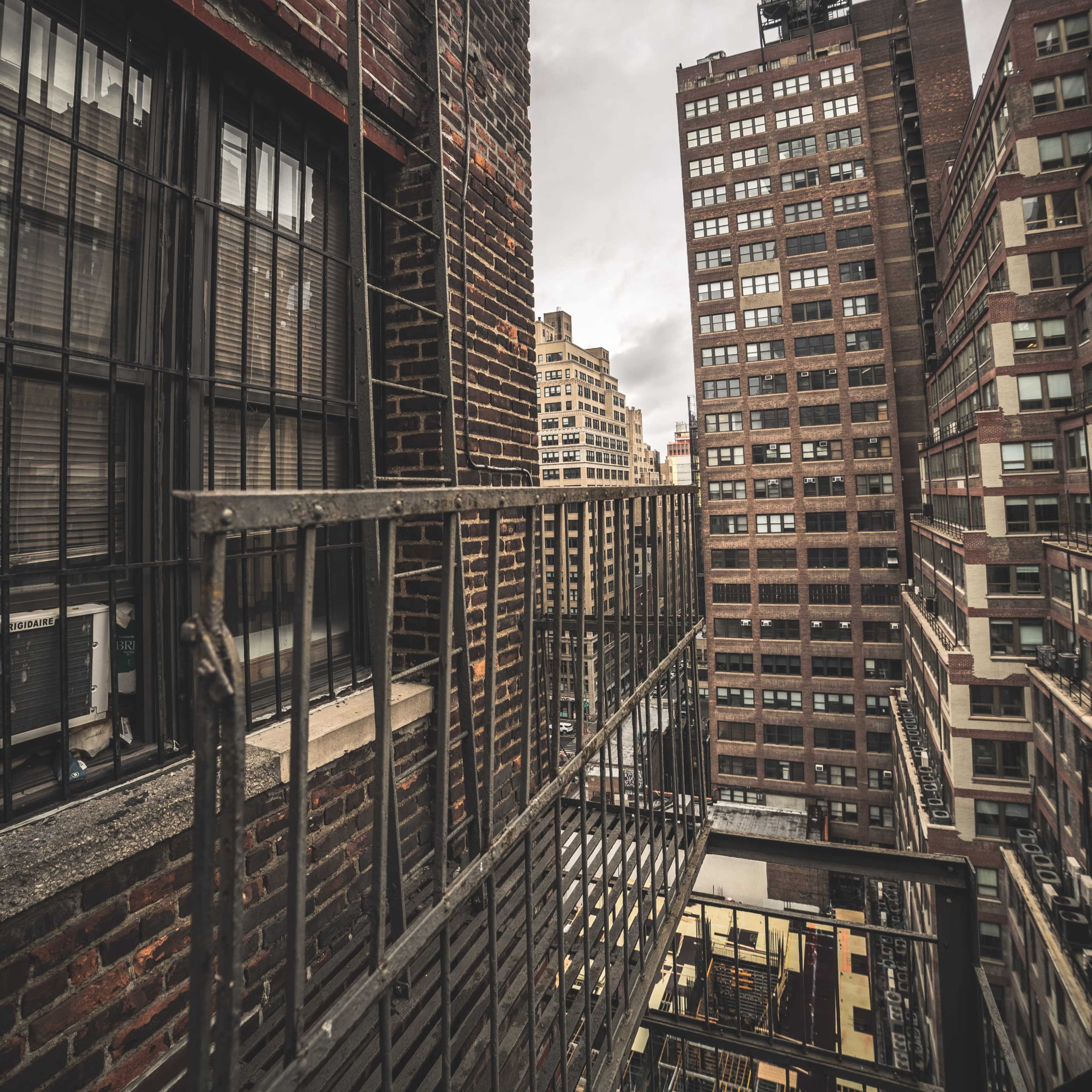 A narrow fire escape on a brick building overlooking a densely packed urban landscape with tall buildings.