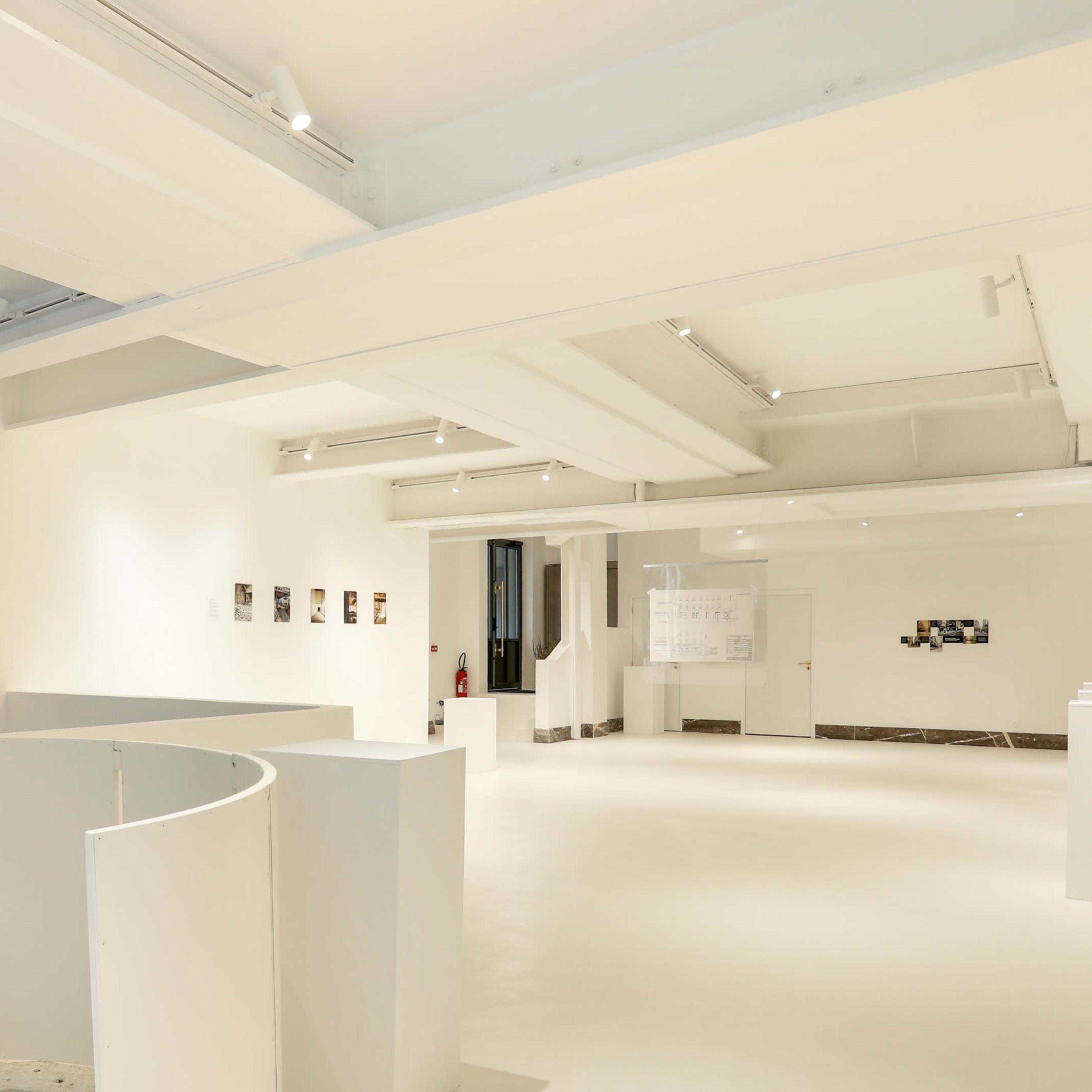 A spacious, modern art gallery with white walls and minimalistic decor, featuring artwork displayed on the walls and a curved structure in the foreground.