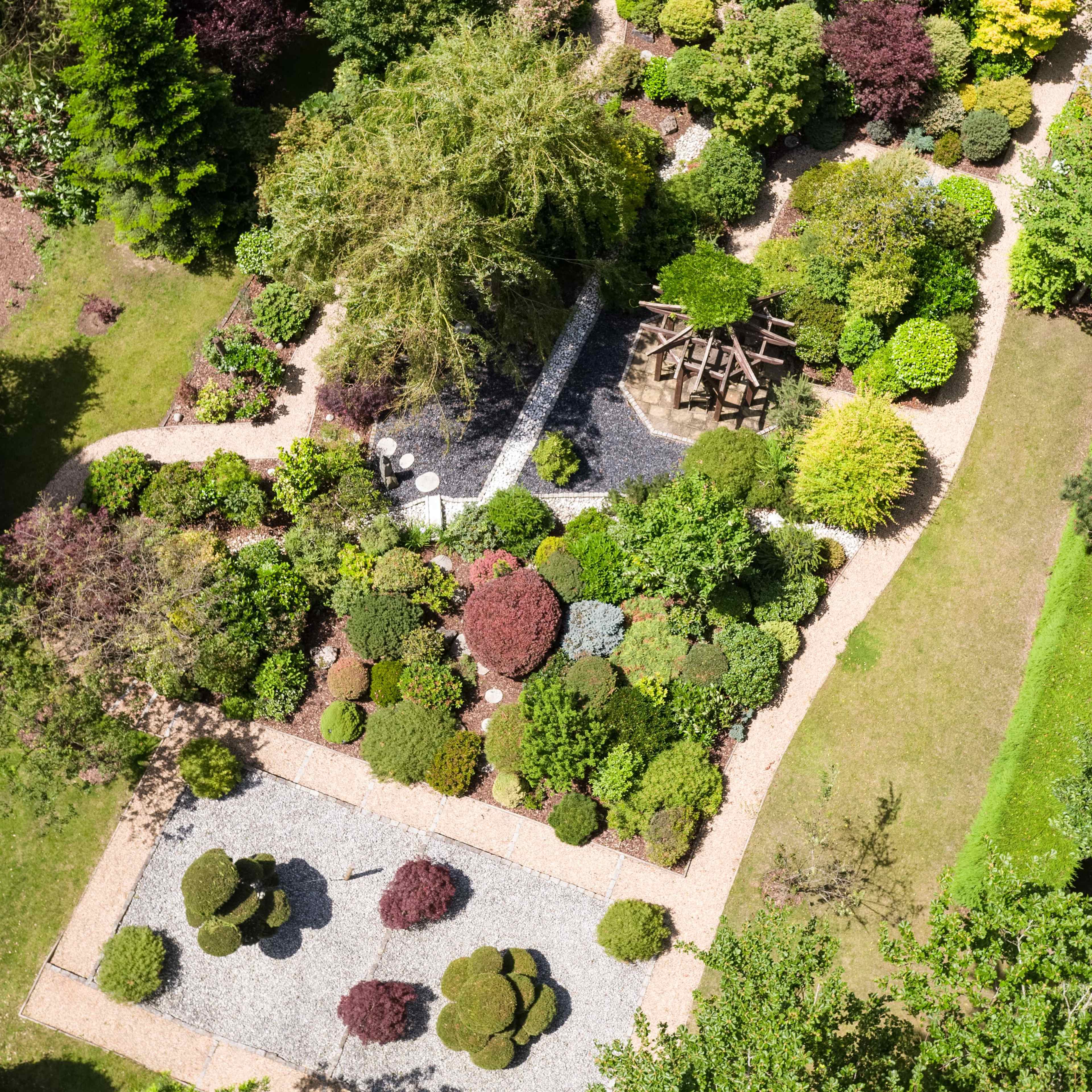 An aerial view of a lush garden featuring meticulously arranged shrubs, pathways, and a wooden structure in the center.
