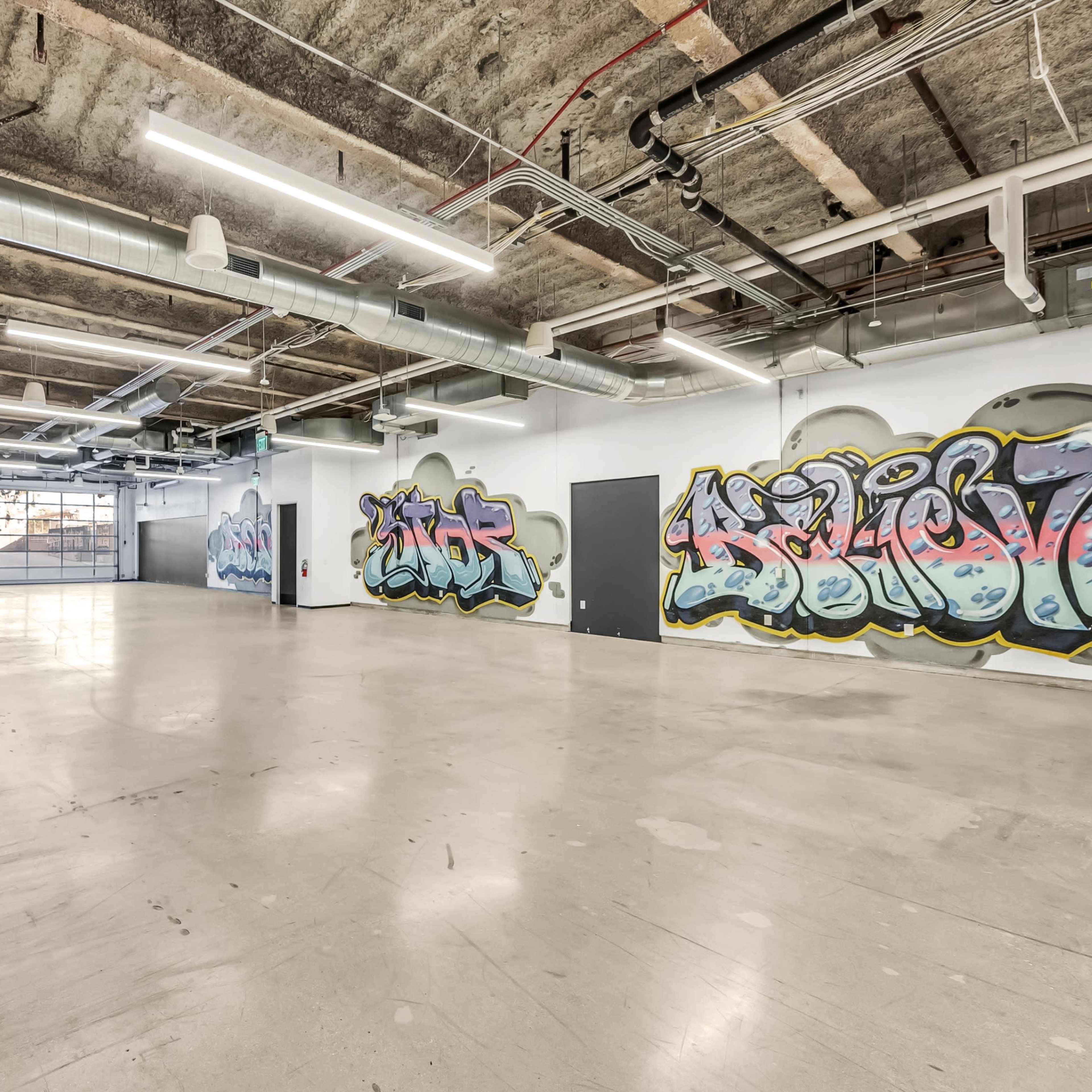 An empty industrial space with exposed concrete walls and graffiti art on two of the walls.