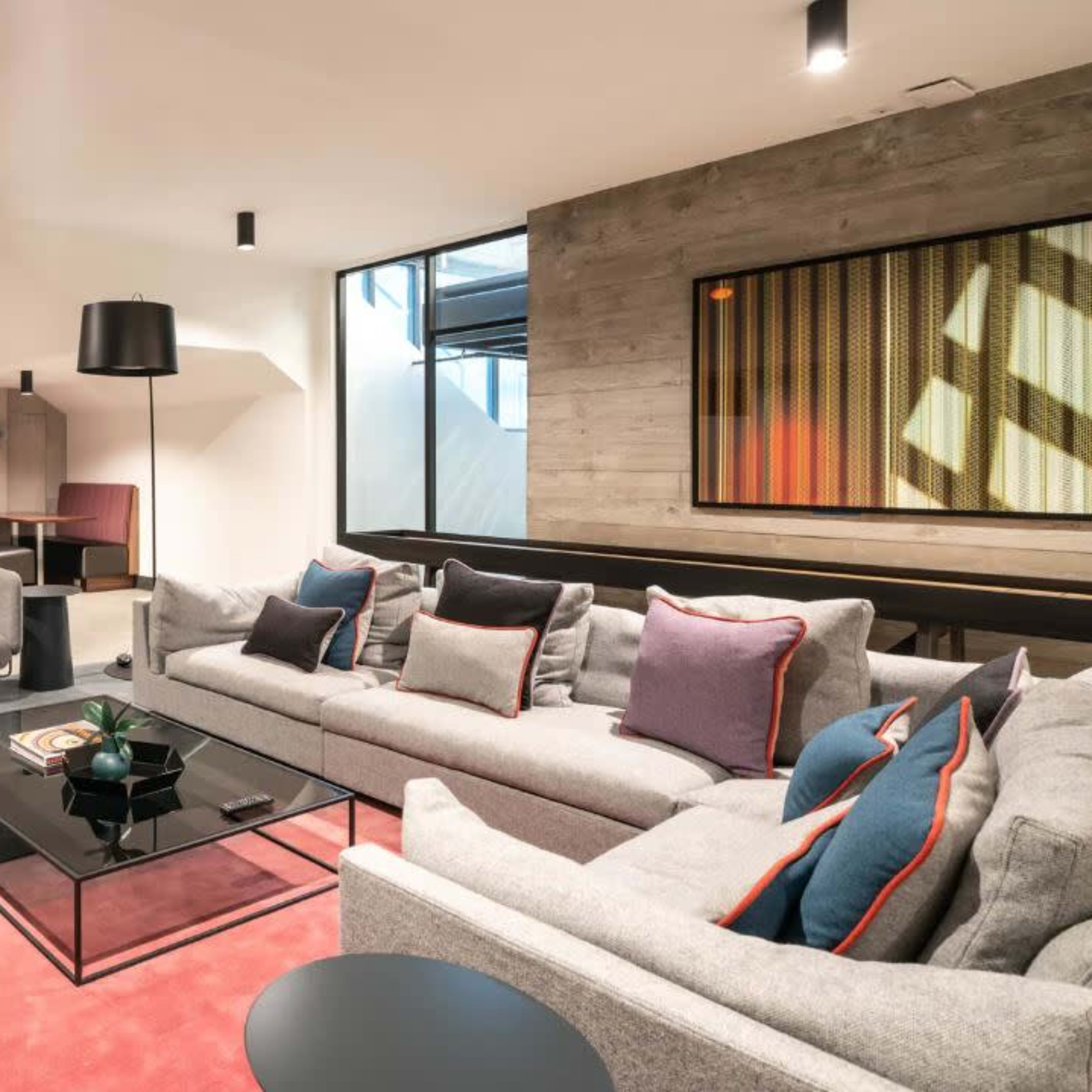 A modern living room featuring a gray sectional sofa, a glass coffee table, and large windows with a view of a dining area in the background.