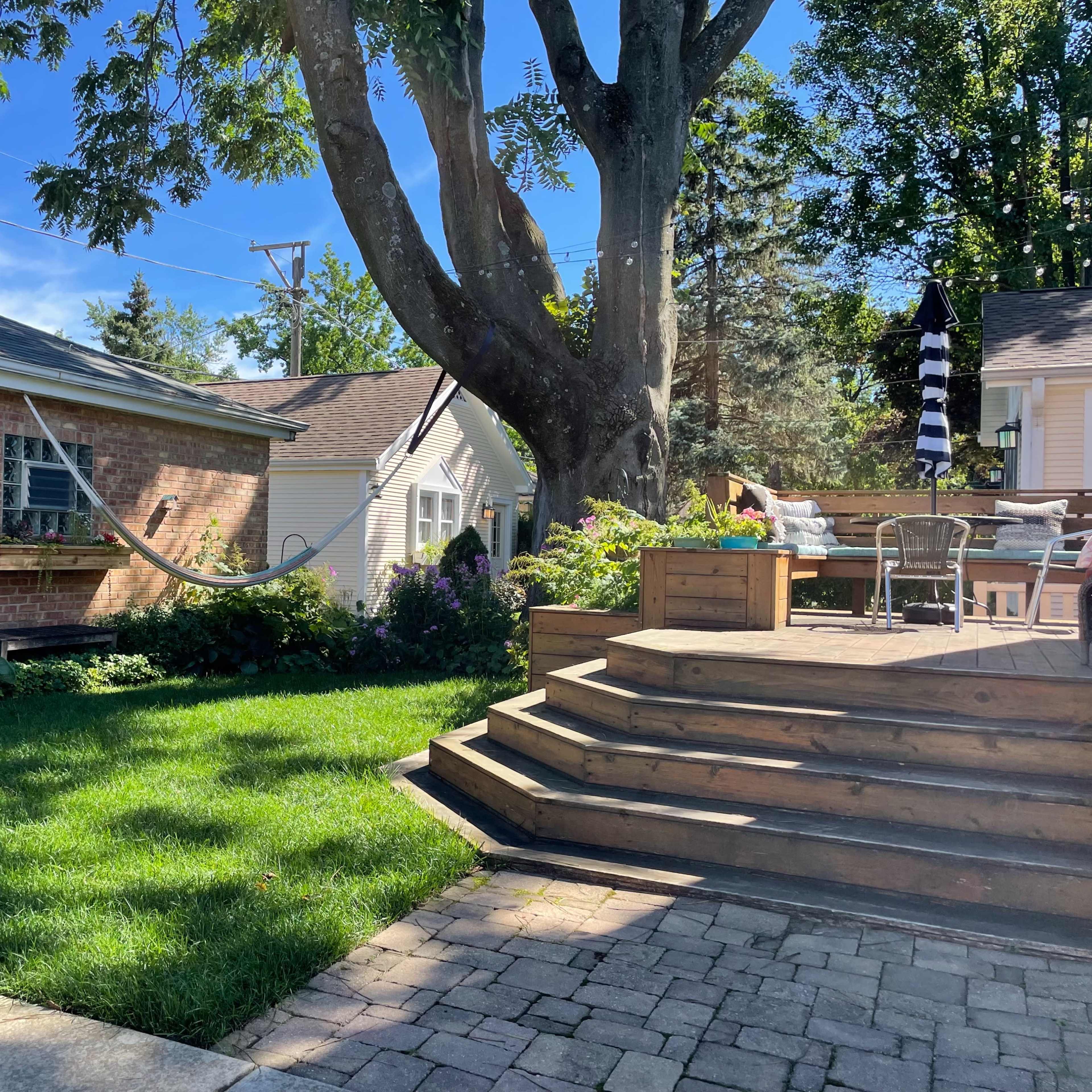 A backyard scene features a large tree, a hammock strung between two structures, and a wooden deck with outdoor furniture.