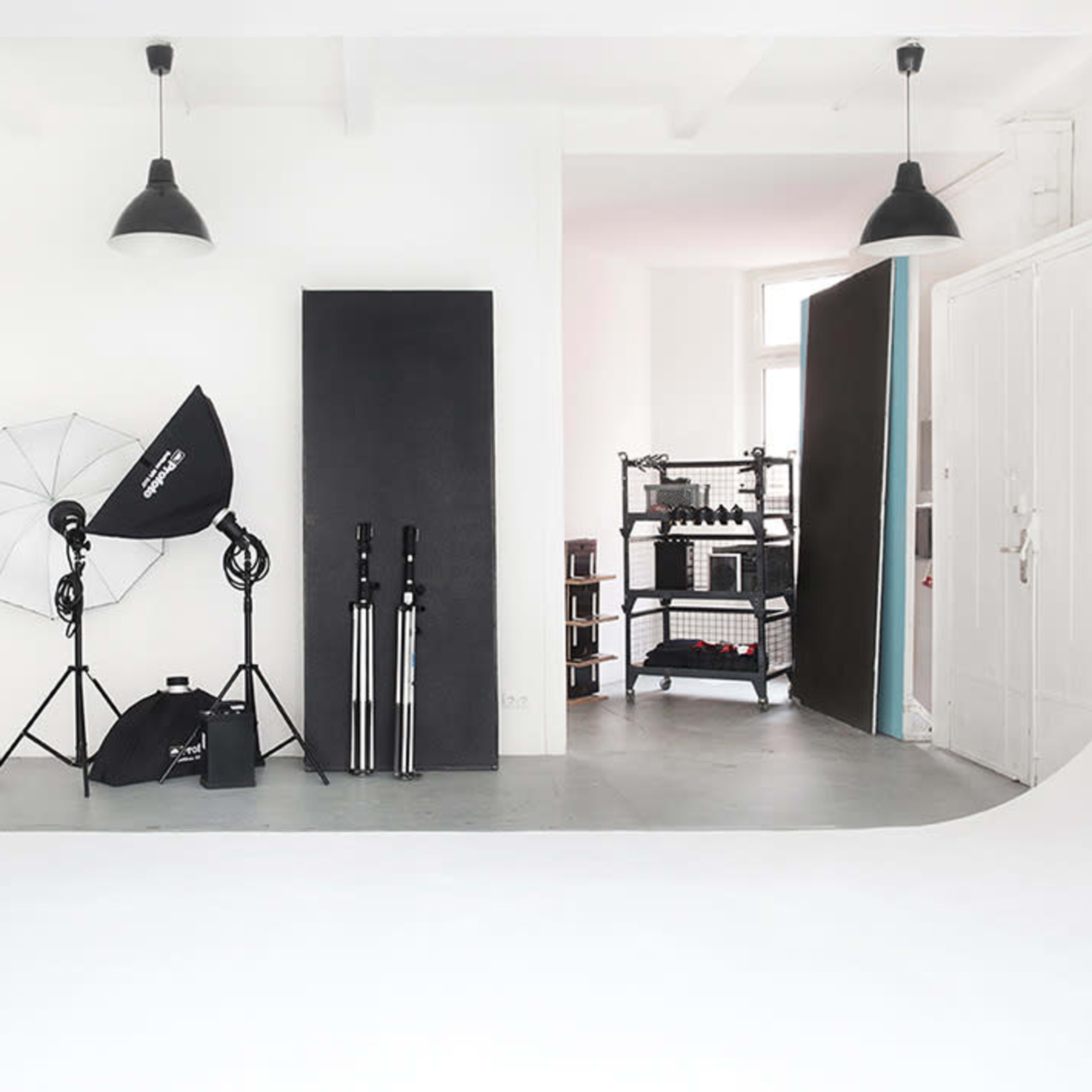 A minimalistic photography studio featuring a backdrop, lighting equipment, a fan, and storage for props.