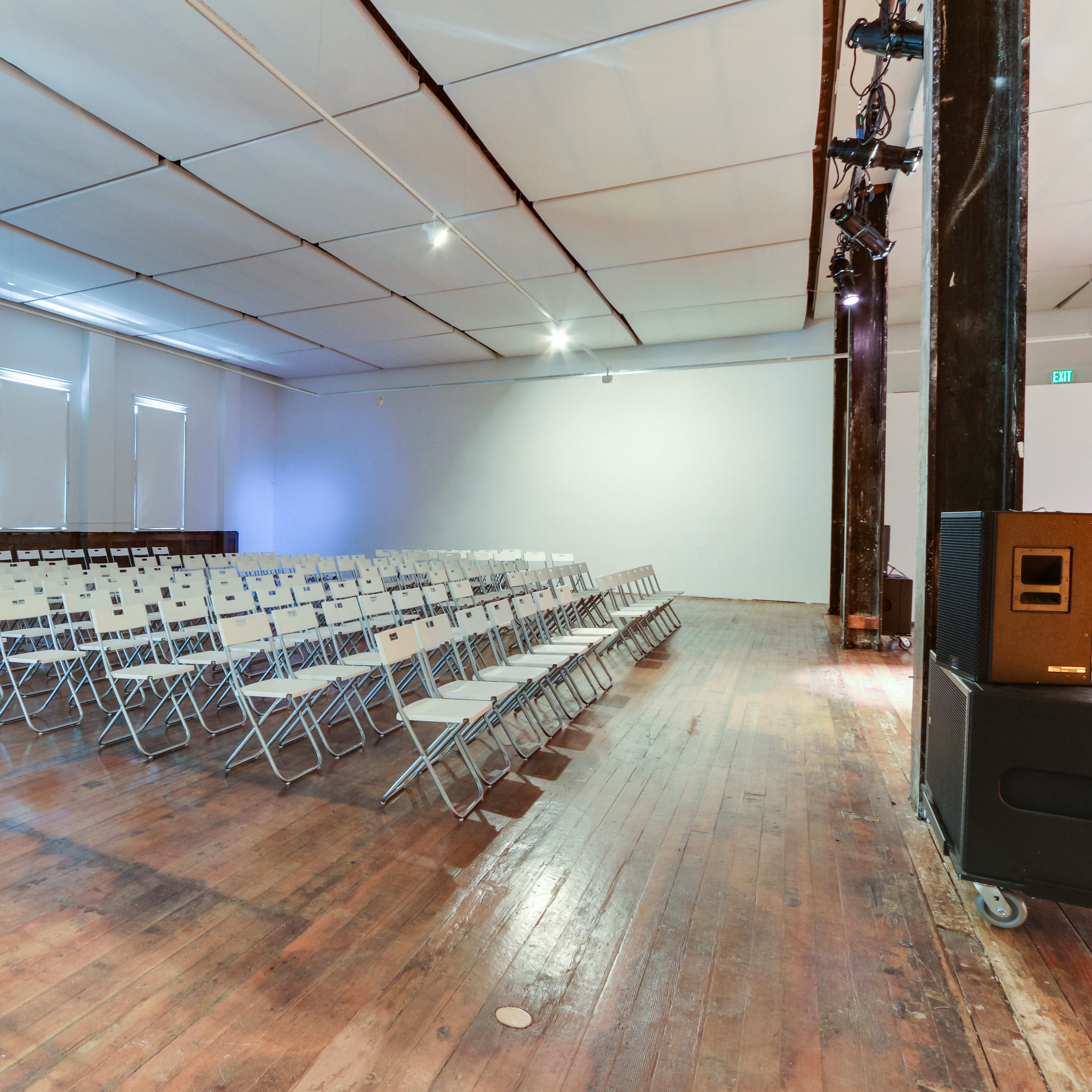 A spacious room with wooden flooring is set up with rows of empty folding chairs facing a blank wall.