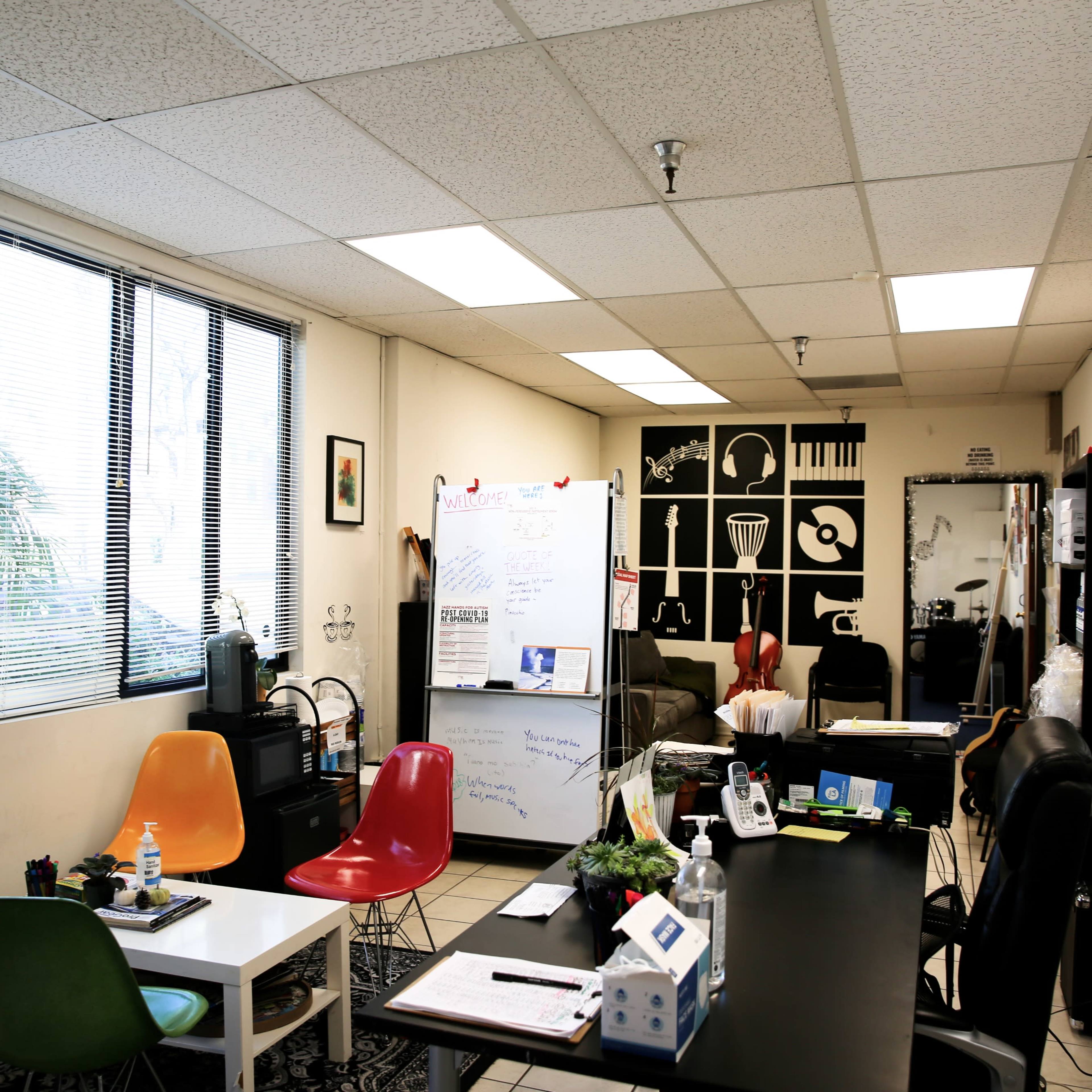 A modern office space features colorful chairs, a large whiteboard, and wall art depicting musical instruments.