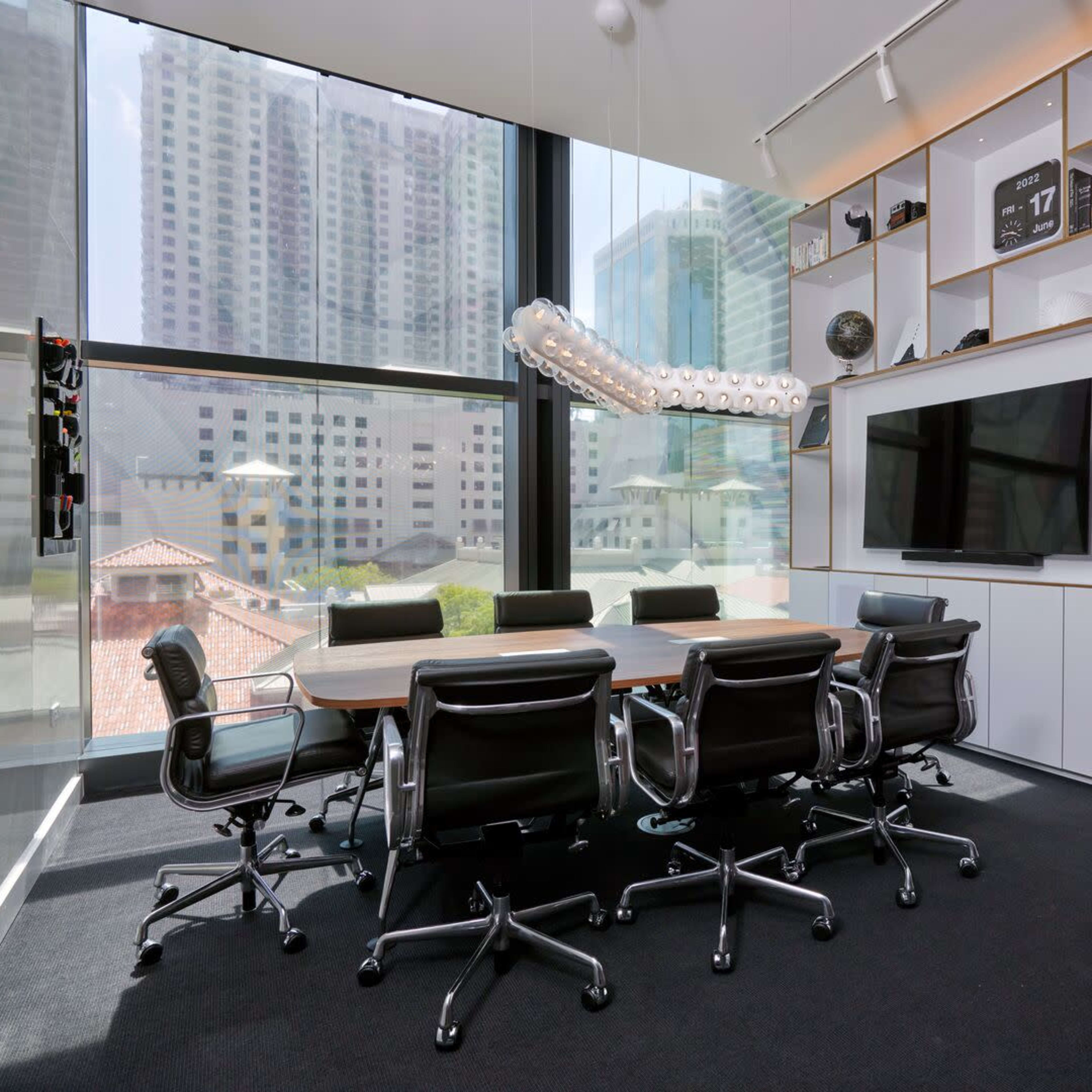 A modern conference room features a large rectangular table surrounded by ergonomic chairs, illuminated by natural light from floor-to-ceiling windows.