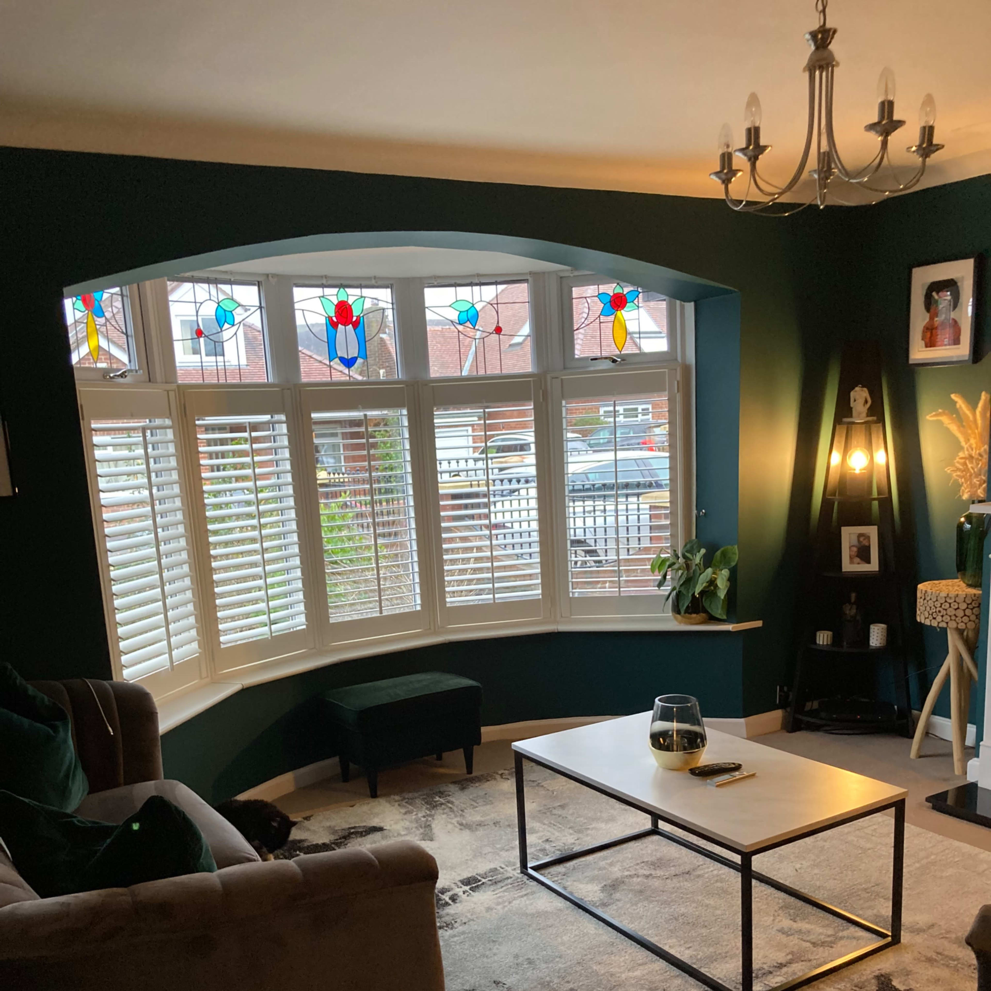 A cozy living room with a curved bay window featuring stained glass, a low coffee table, and a dark green accent wall.
