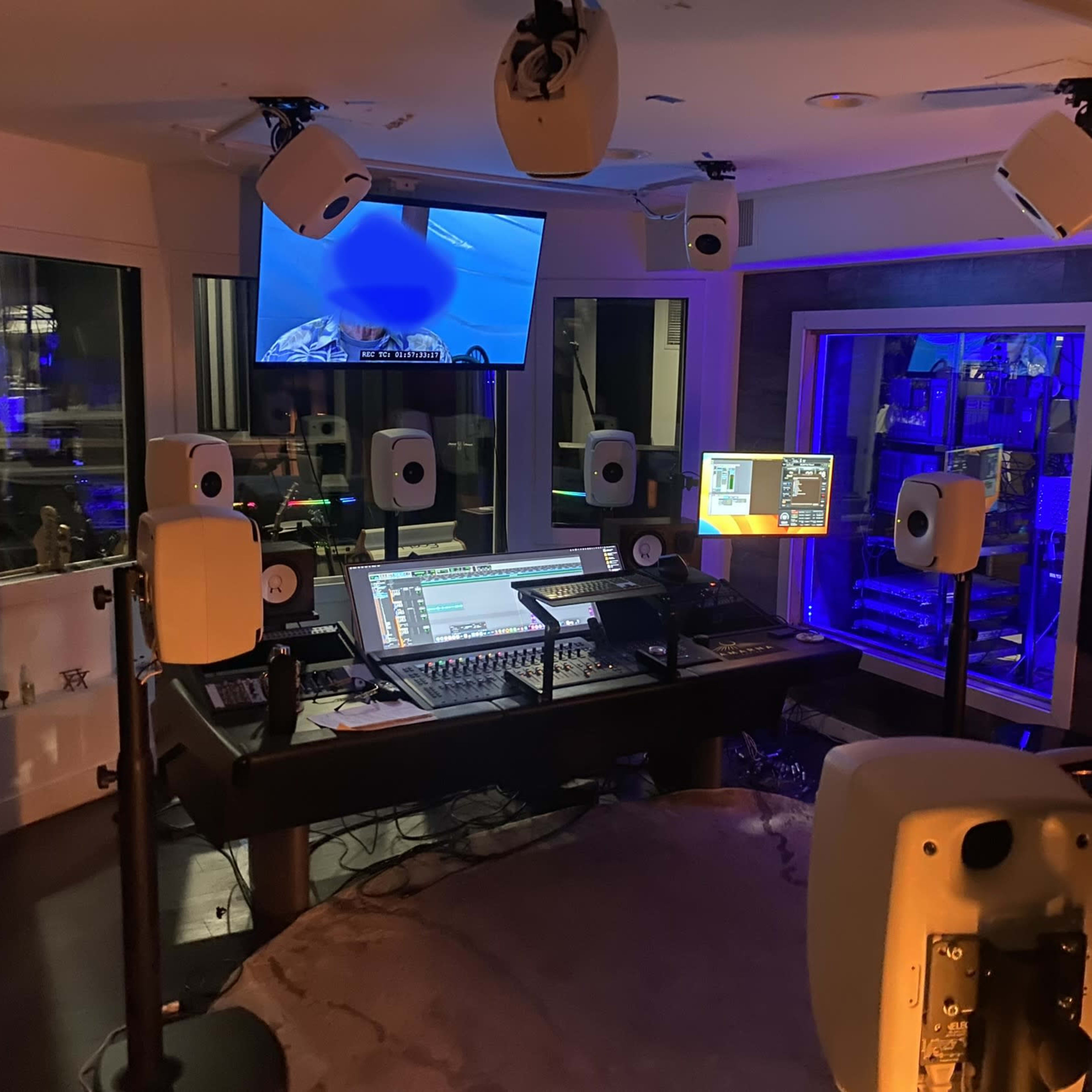 A modern music production studio with multiple speakers, a central mixing console, and a large monitor displaying audio software.