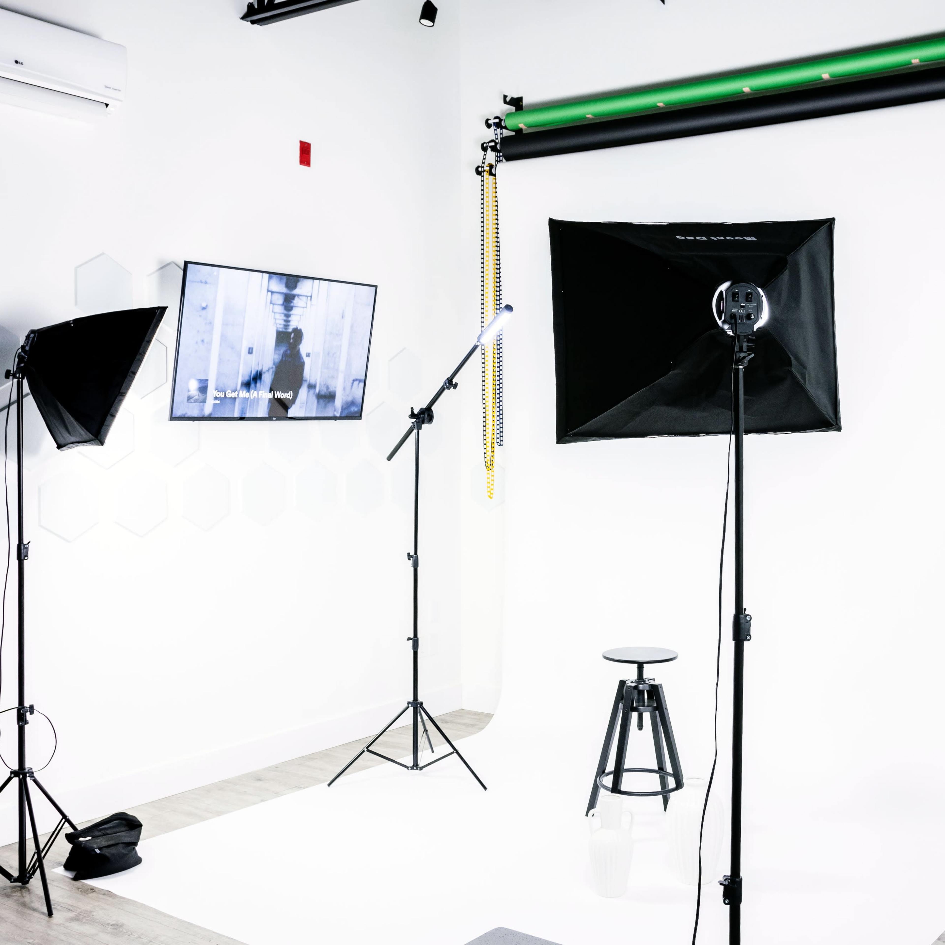 A photography studio setup with a white backdrop, a stool in the center, and various lighting equipment including softboxes and a monitor displaying an image.