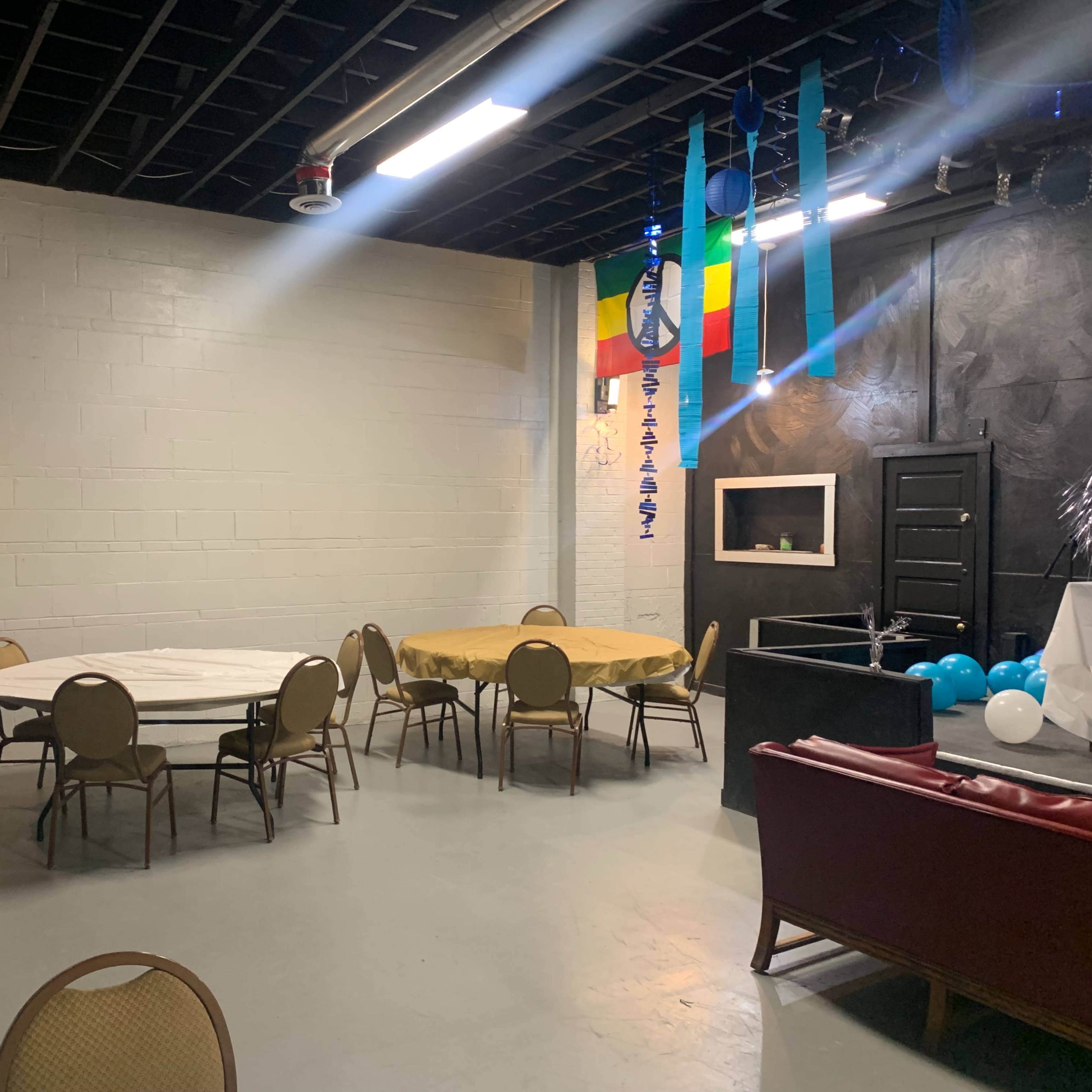An event space with several round tables, a sofa, and decorations hanging from the ceiling.