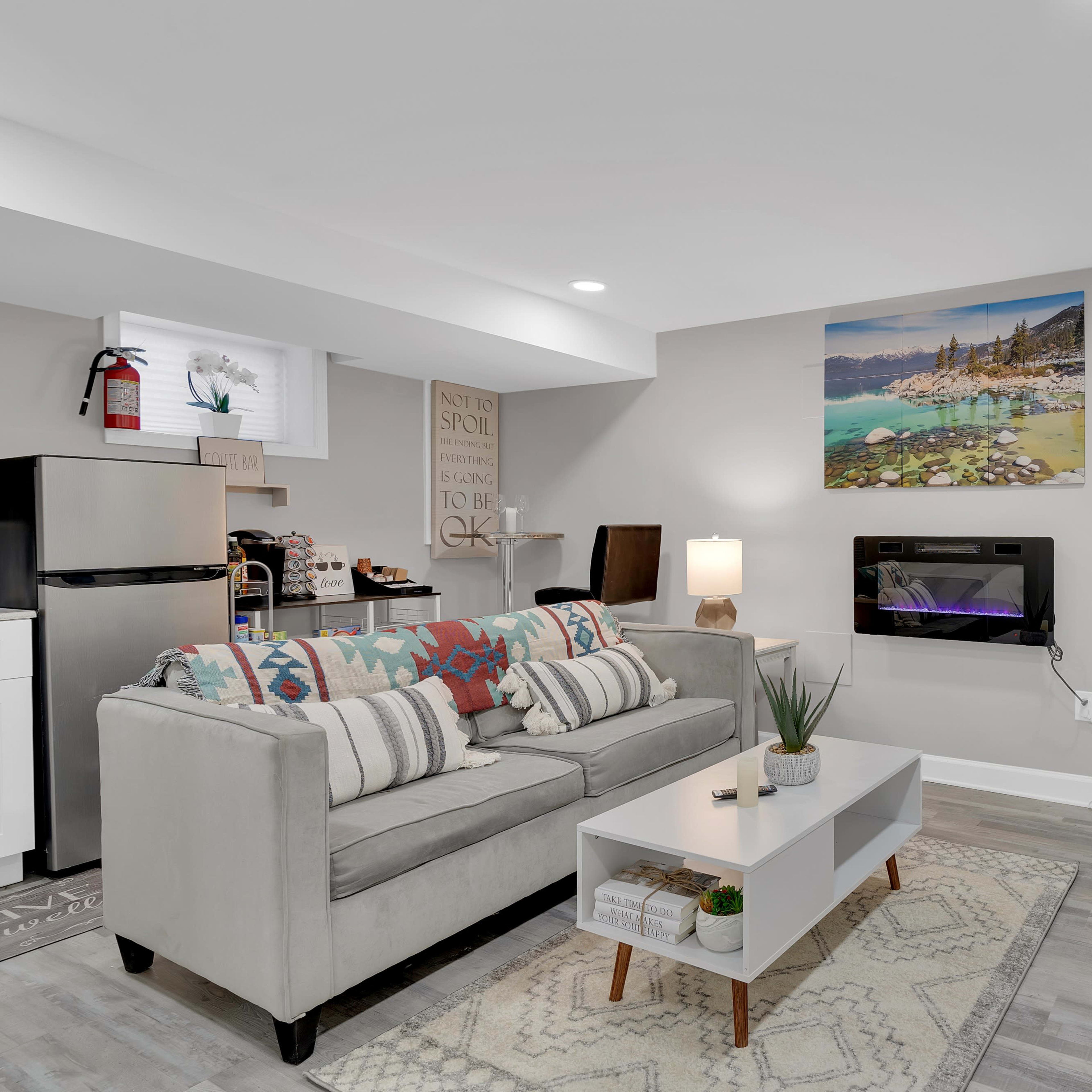 A modern living room with a light gray sofa, a coffee table, a wall-mounted TV, and a decorative plant, complemented by a painting of a coastal scene.