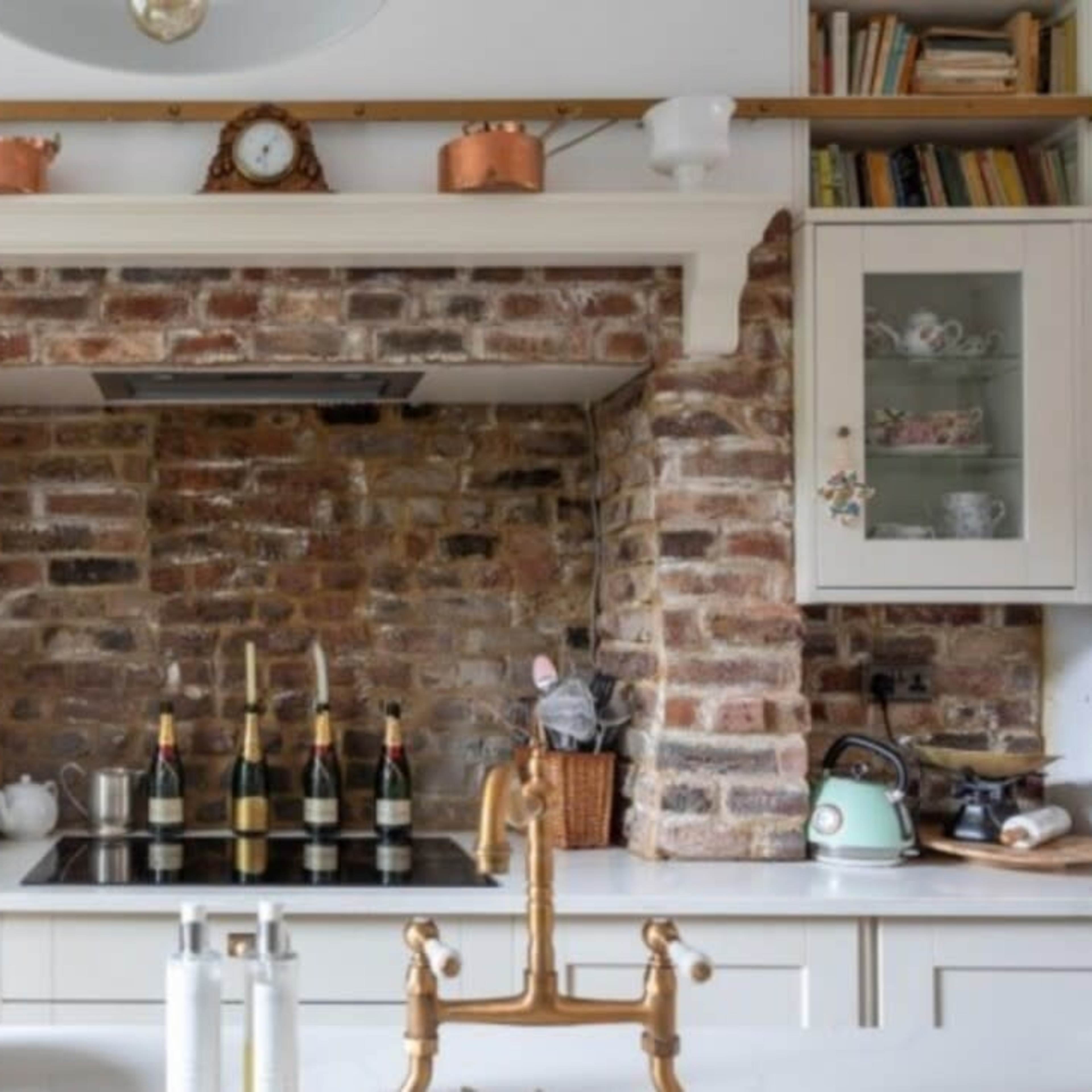 A kitchen with a brick feature wall, a stove, and a wooden ladder leaning against the cabinets.