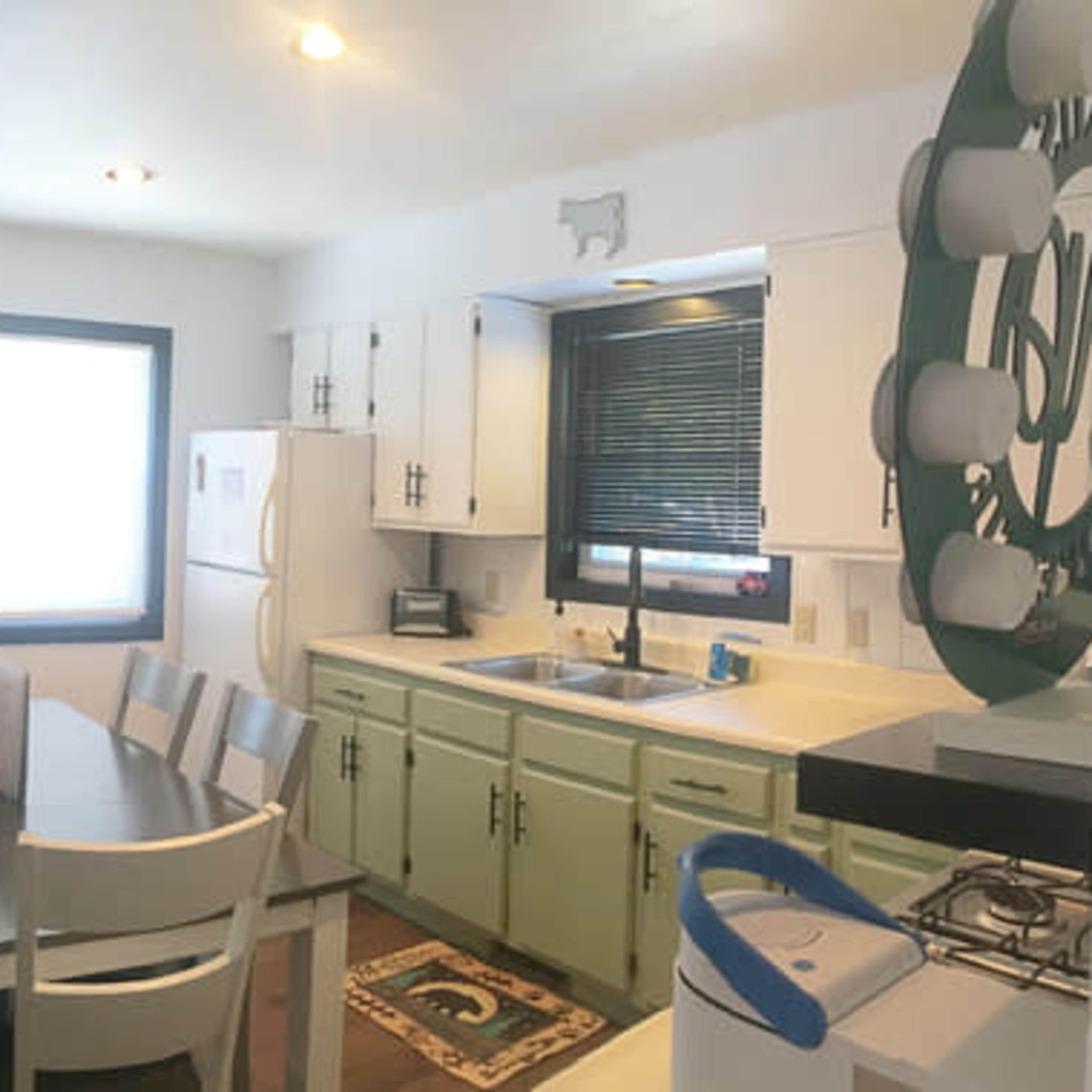 A panoramic view of a living area and kitchen with a sofa, television, dining table, and appliances in a well-lit space.