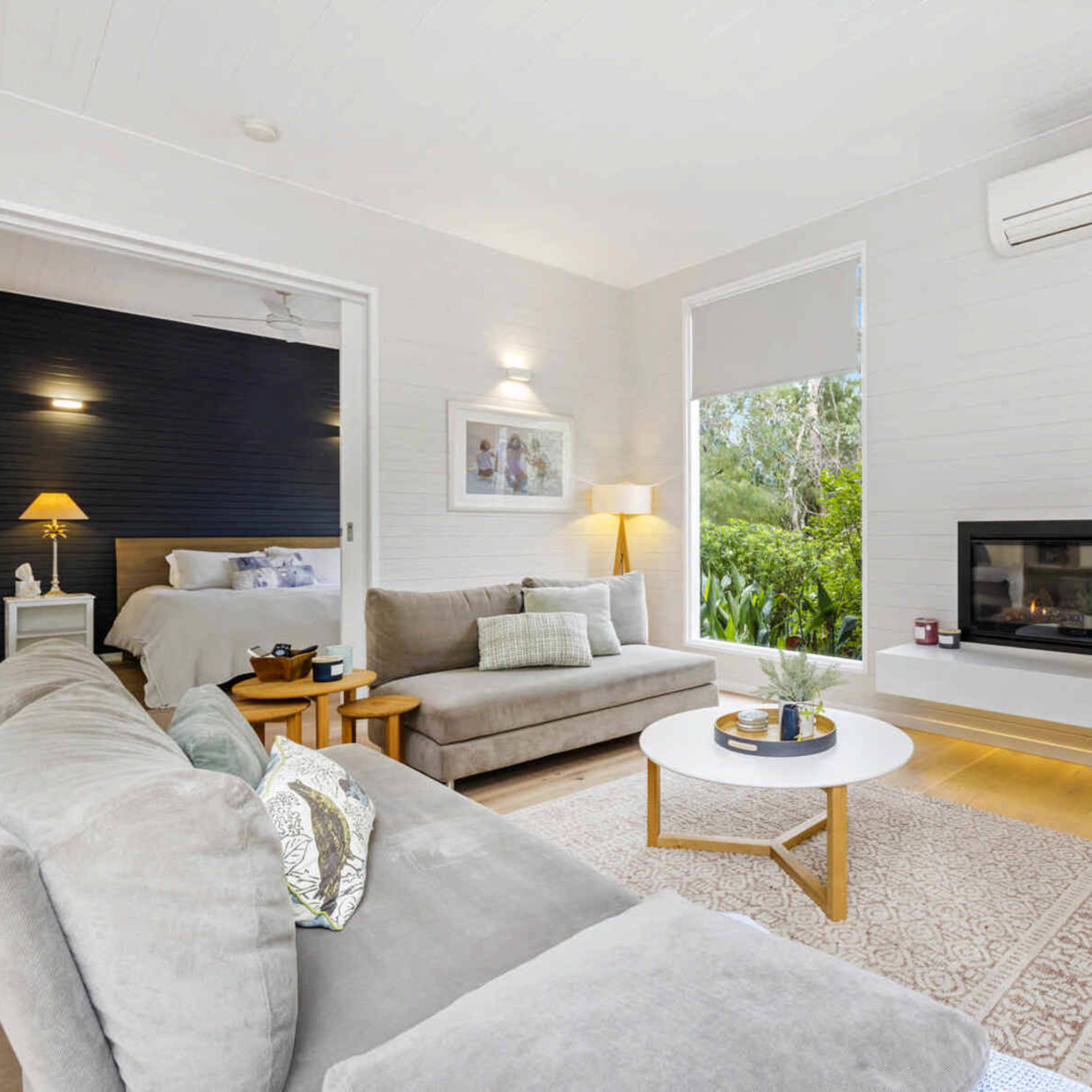 A modern living room with a gray sofa, a round coffee table, and a television mounted on the wall, adjacent to a bedroom area.