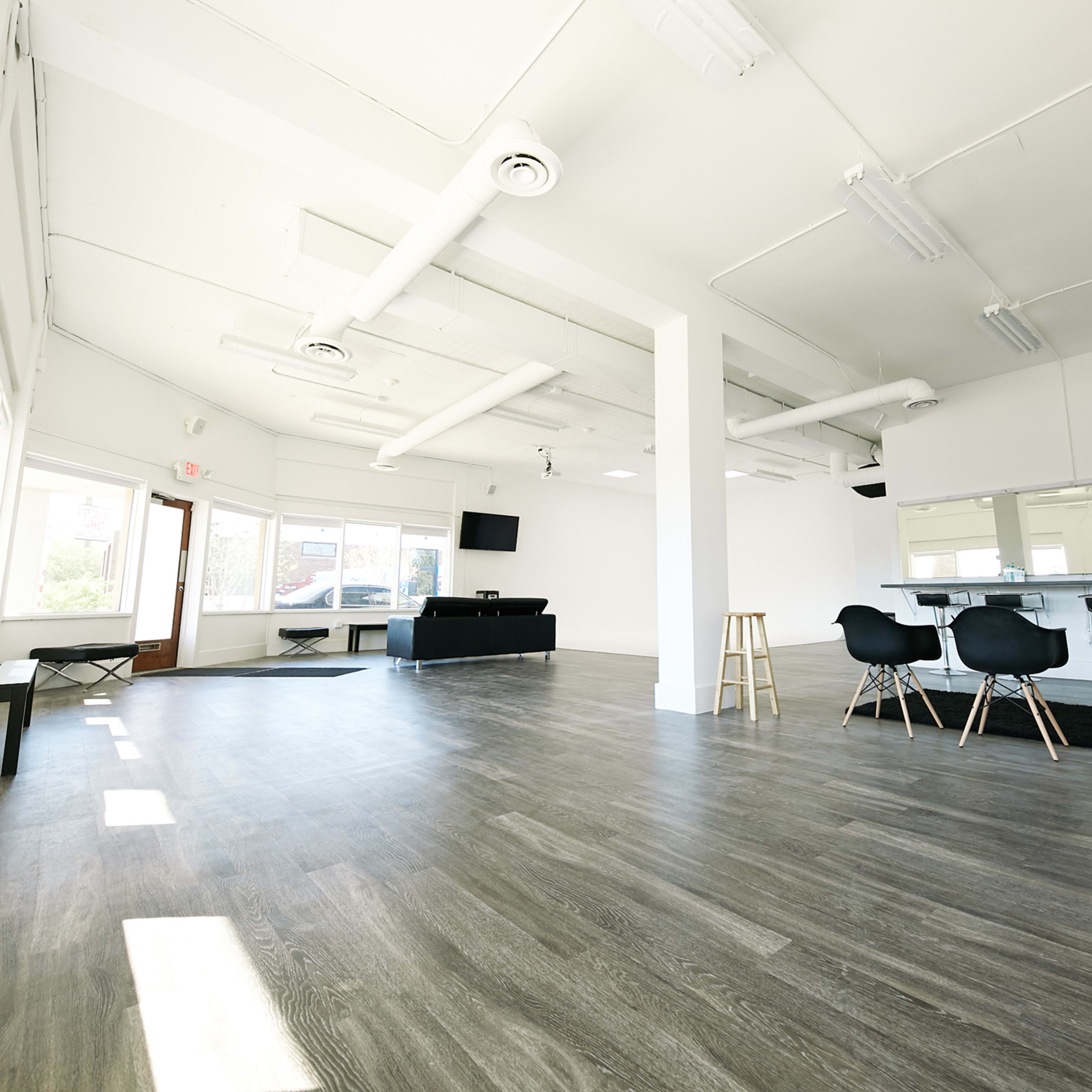 A spacious, well-lit interior with a modern, minimalistic design featuring chairs, mirrors, and large windows.
