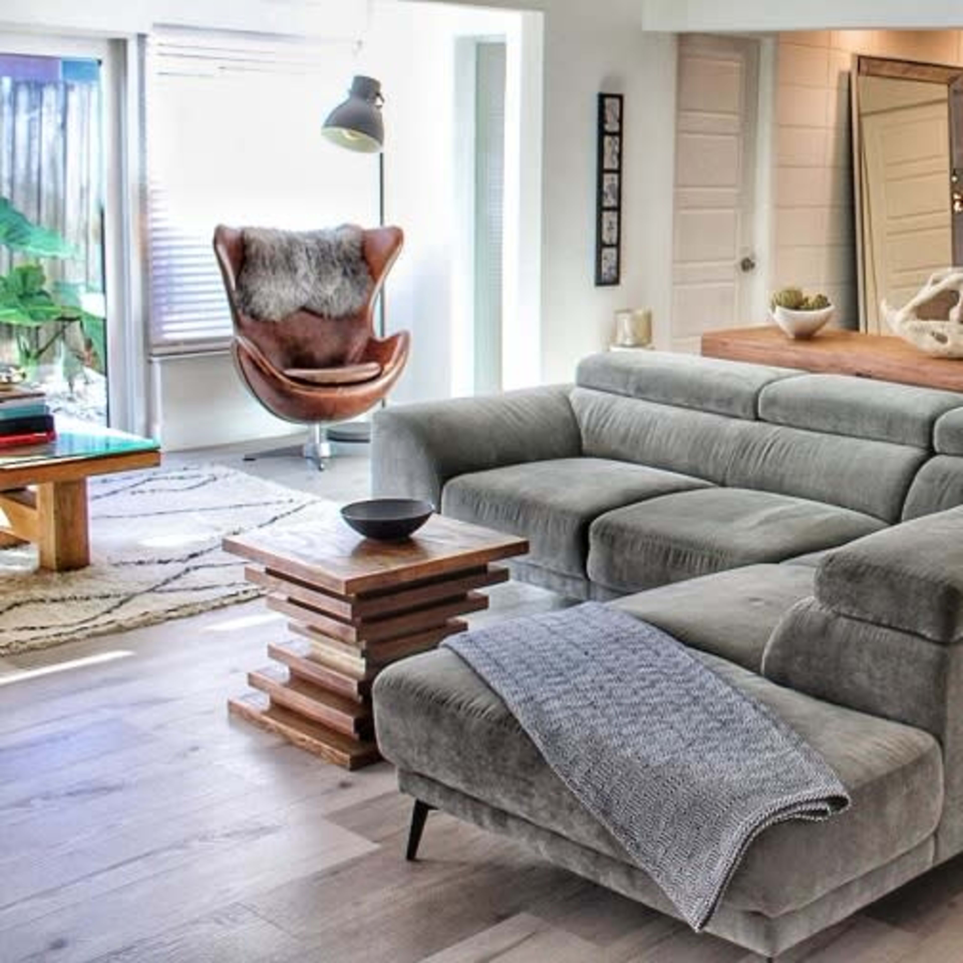 A modern living space with a grey sectional sofa, a wooden dining table, and a decorative light fixture overhead.
