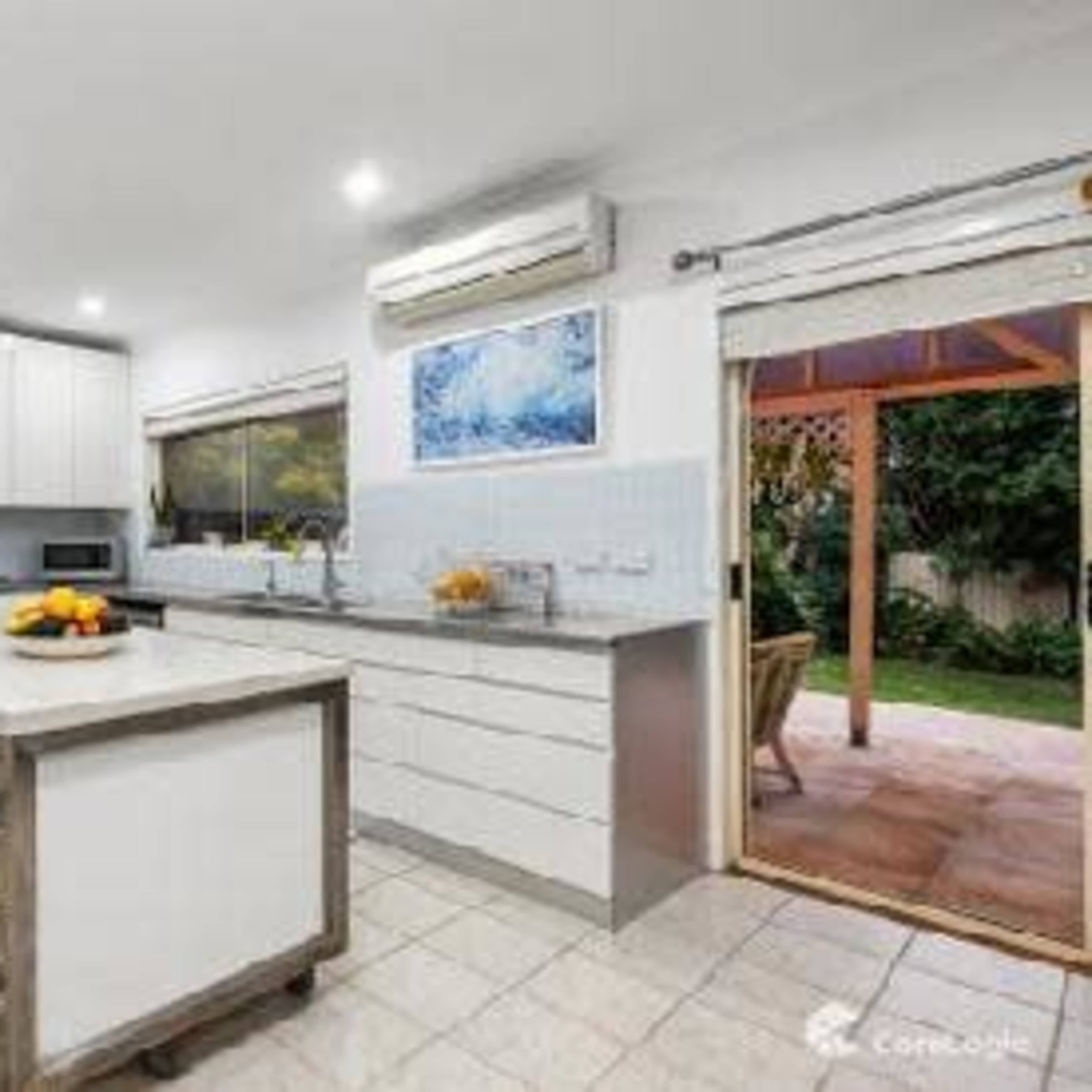 A modern kitchen features white cabinetry, a central island with bar stools, and sliding doors leading to an outdoor patio.