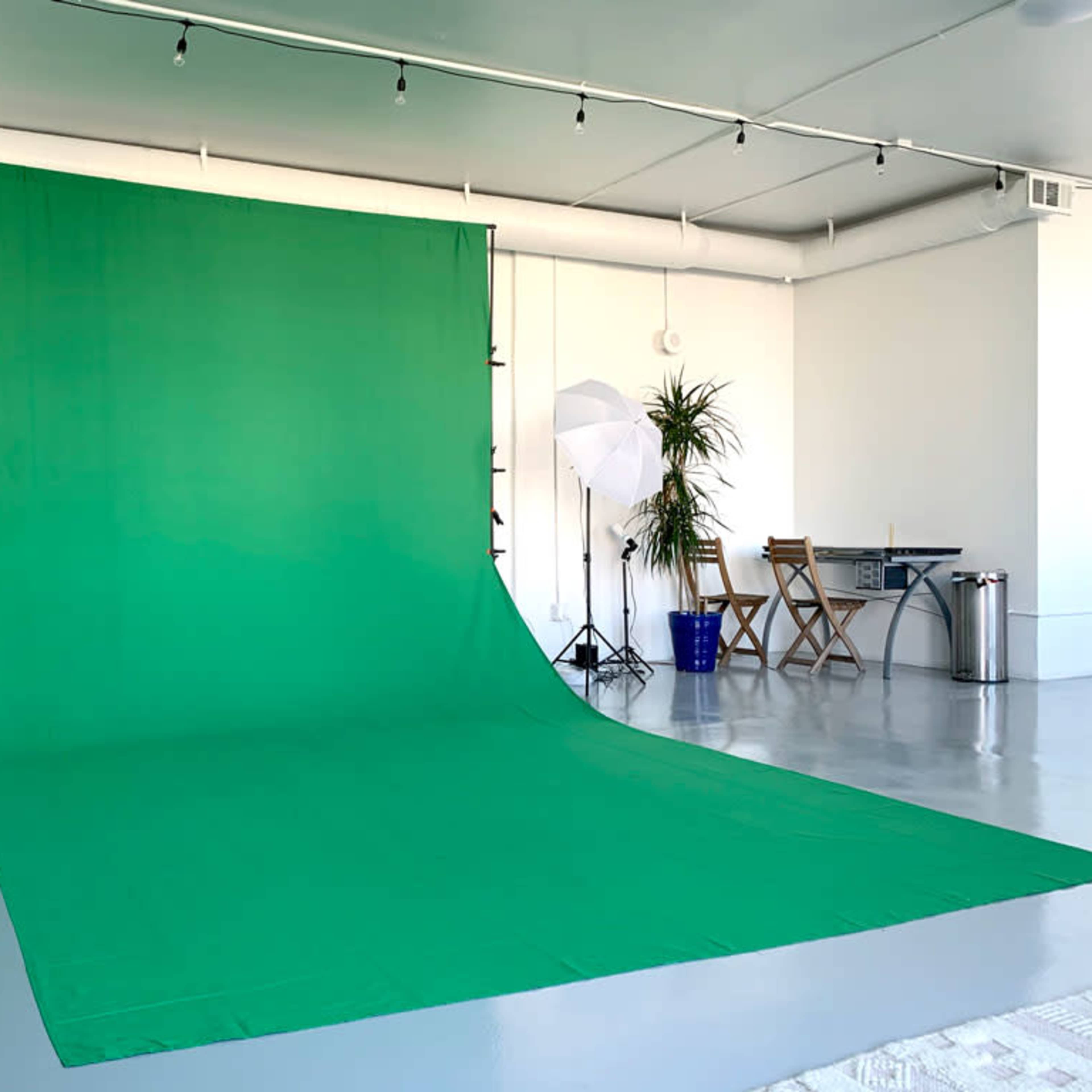 A bright green backdrop set up in a minimalist studio with two softbox lights and furniture arranged nearby.