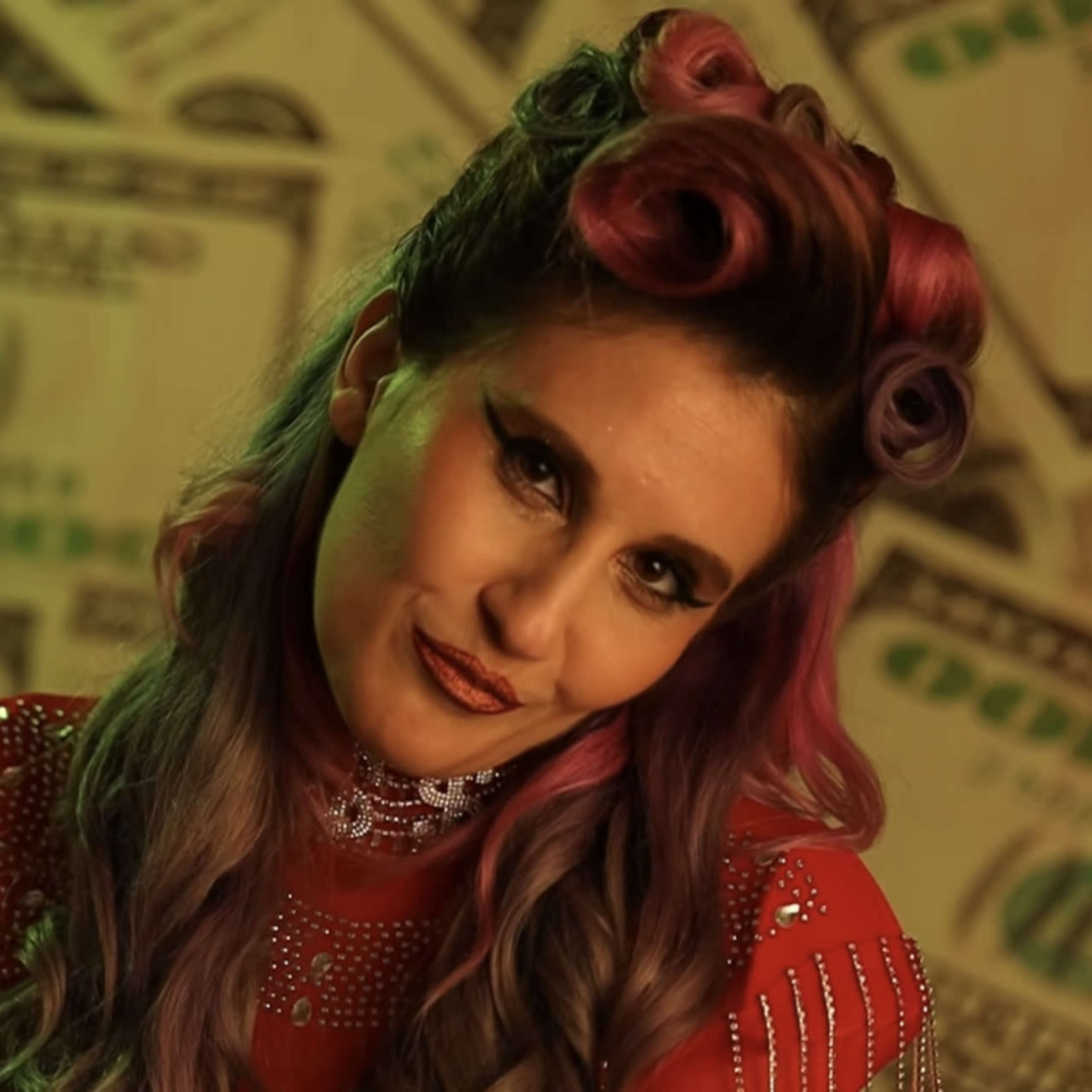 A woman with pink curls holds a toy gun in front of a backdrop covered in images of money.
