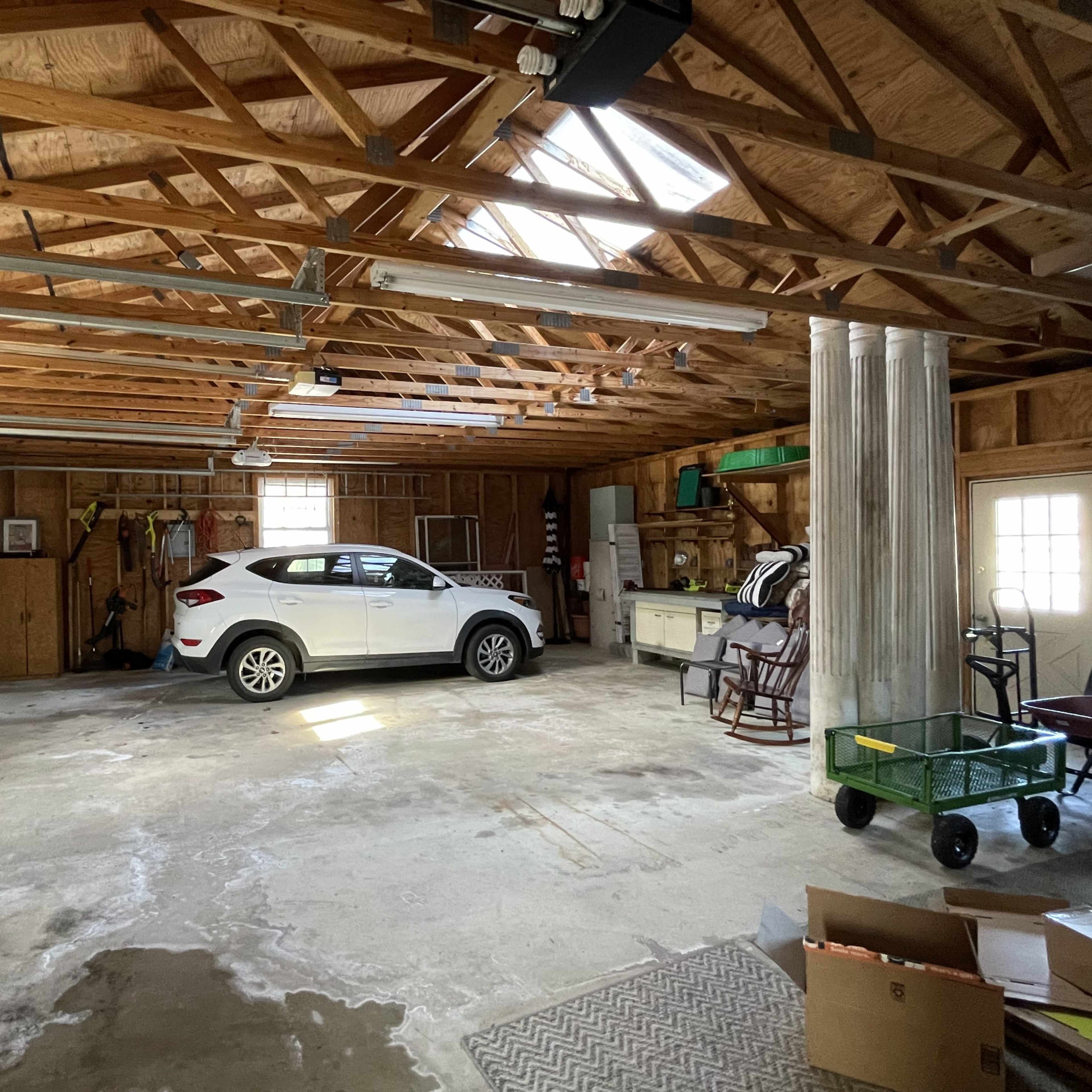 A white car is parked inside a spacious garage with wooden walls, exposed beams, and a concrete floor.