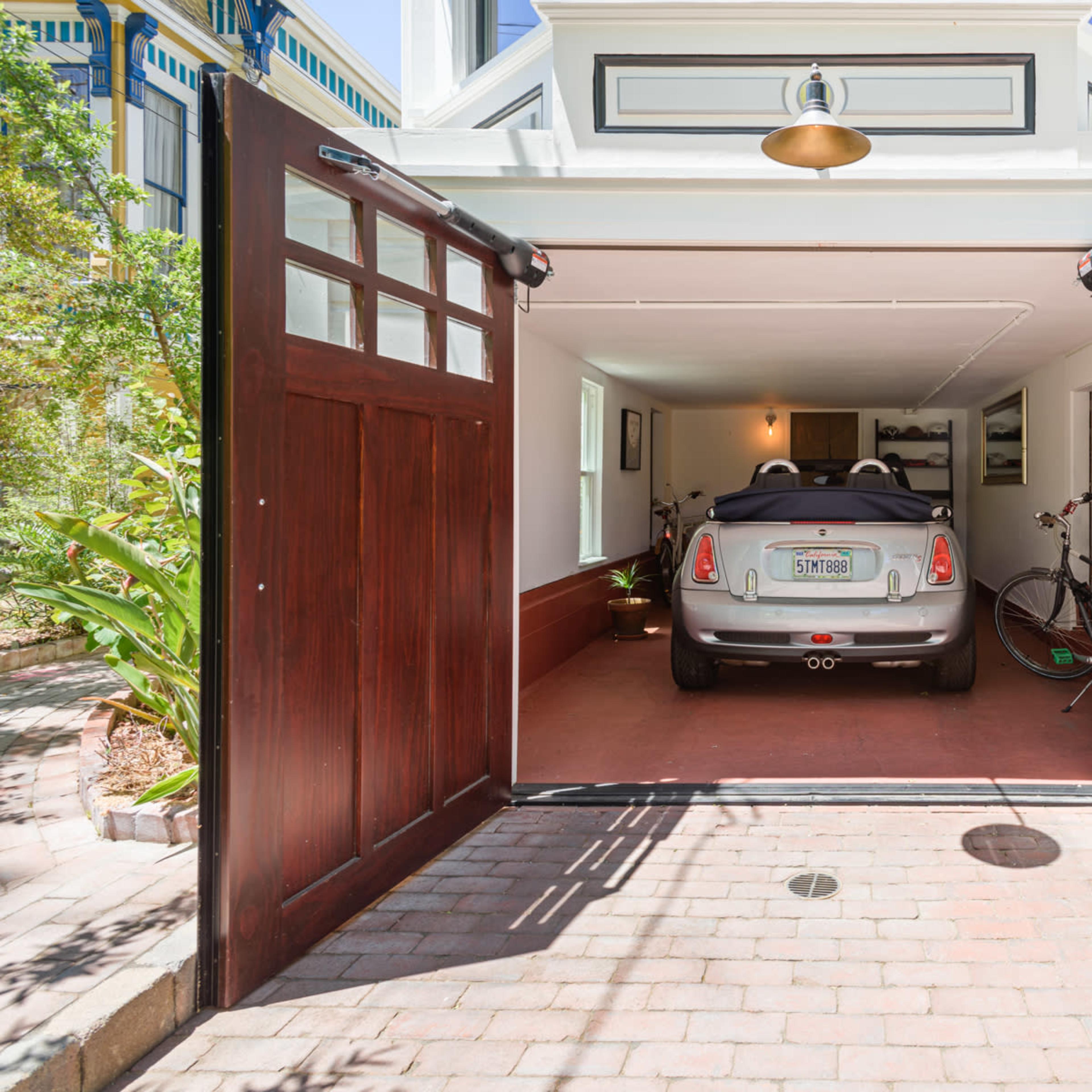 A compact car is parked inside a spacious garage with wide wooden doors, accompanied by a bicycle on the side.