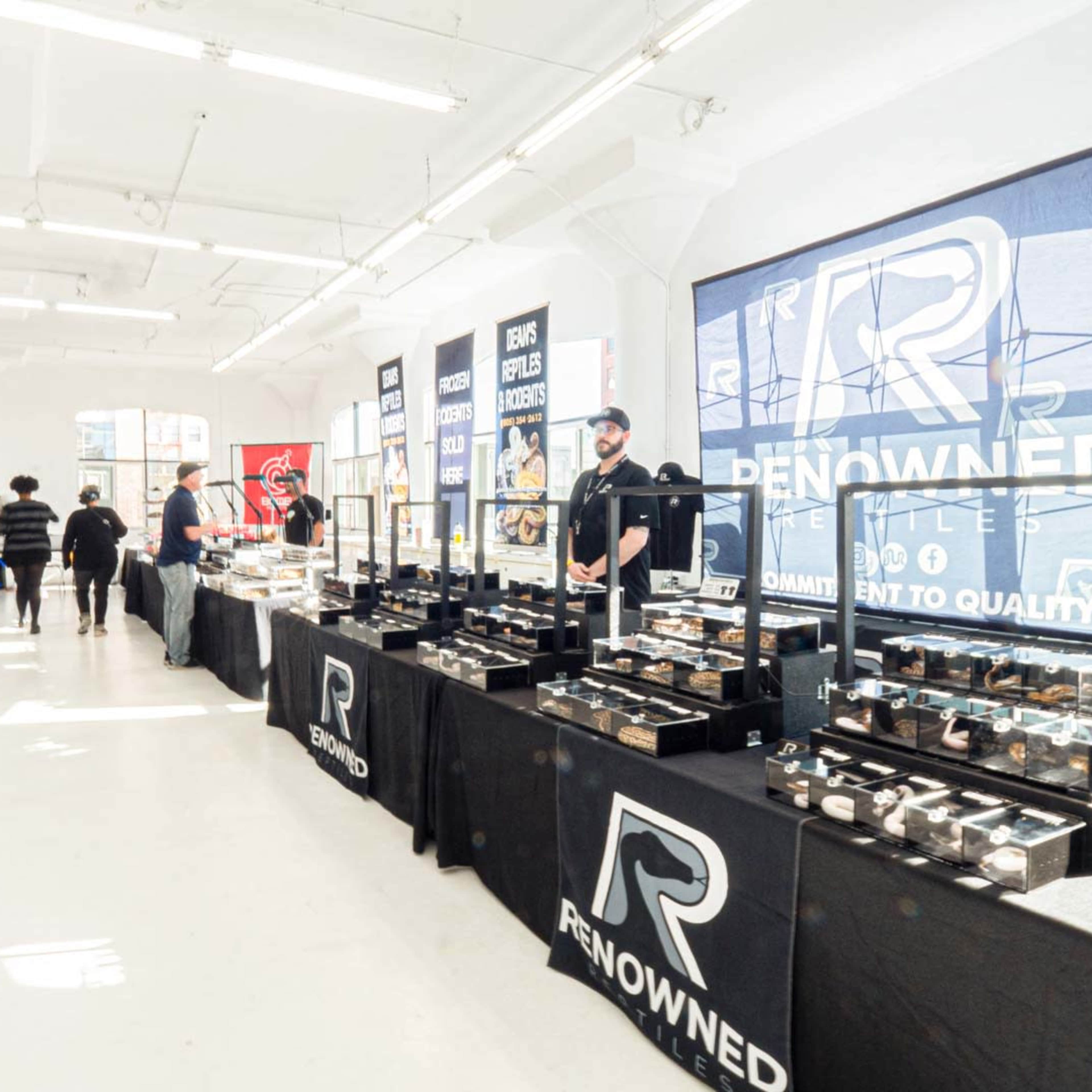 A bustling indoor market setup featuring vendor tables displaying various jewelry pieces and branded signage.