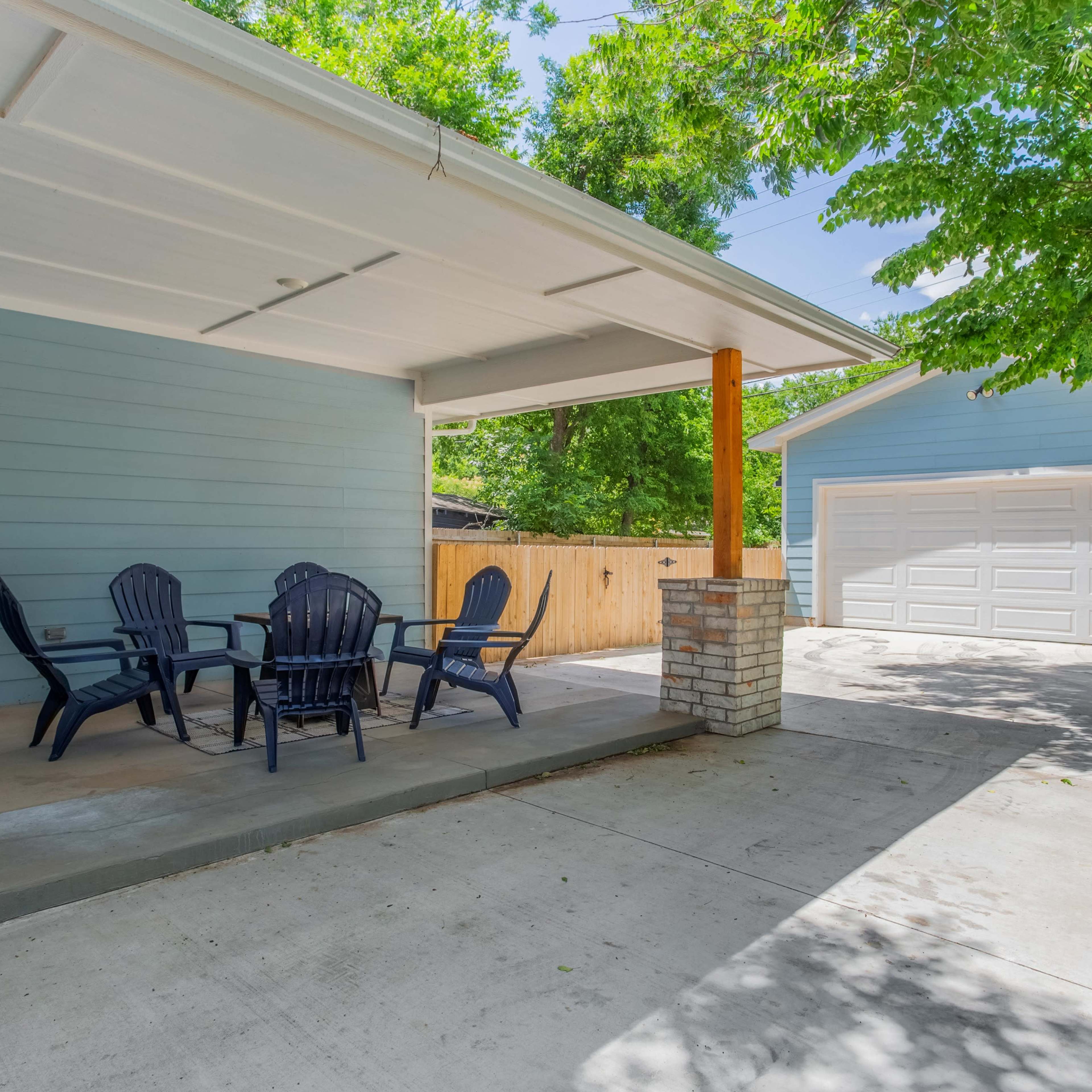 A patio with black outdoor furniture is situated next to a driveway leading to a two-car garage.