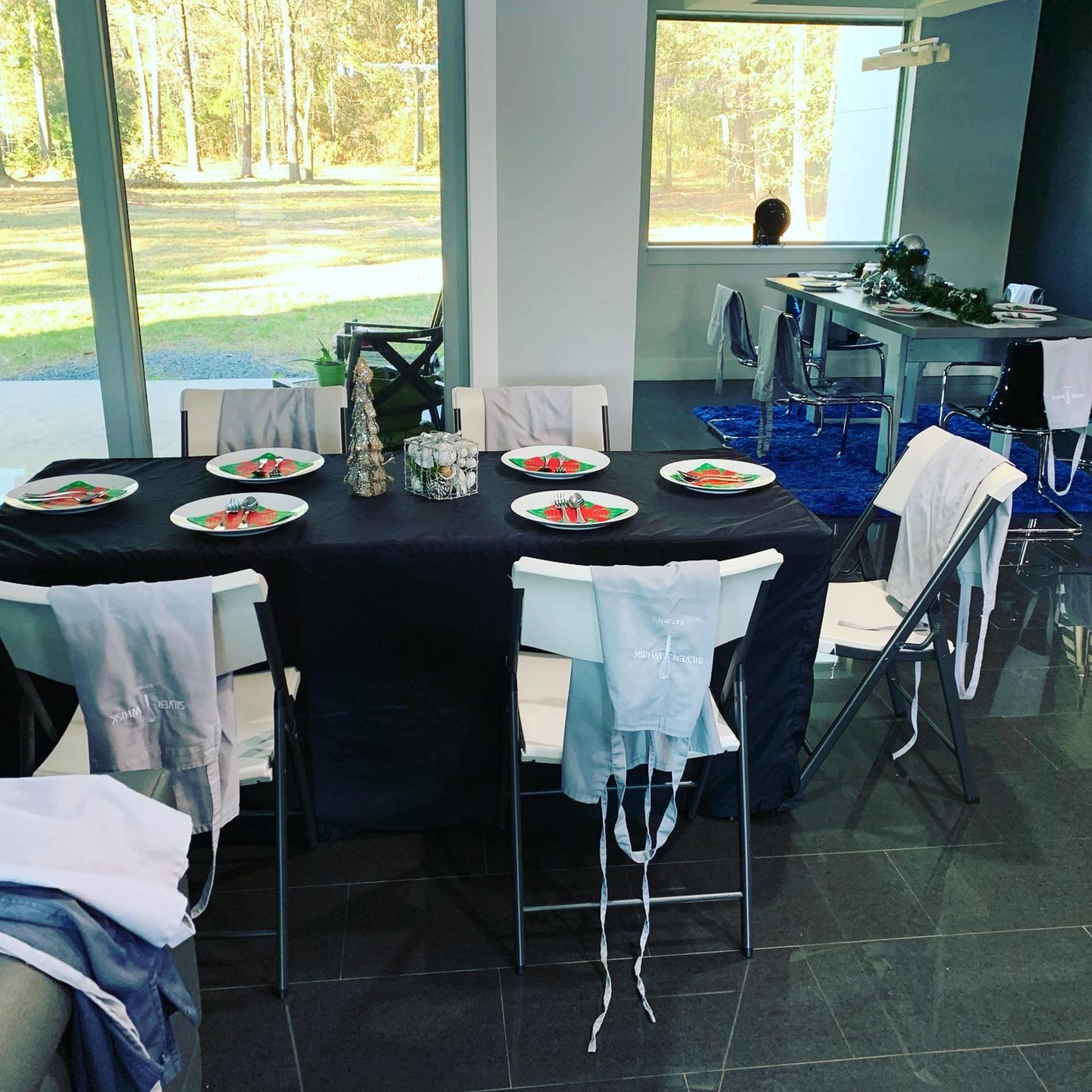 A dining table is set with plates of food, surrounded by folding chairs and adorned with decorative items in a modern room with large windows.