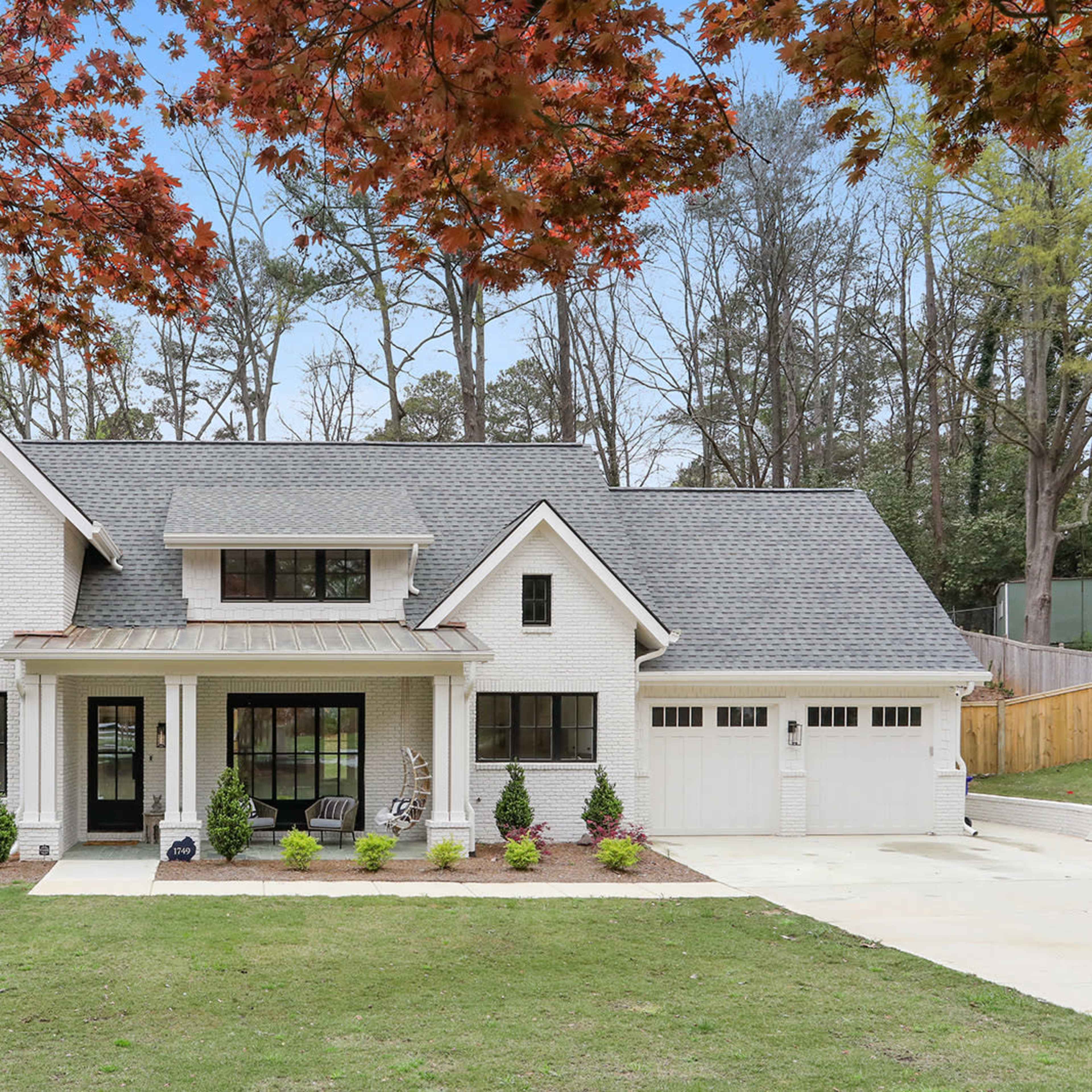 A white brick house with a gray roof, large windows, and a manicured lawn surrounded by trees.