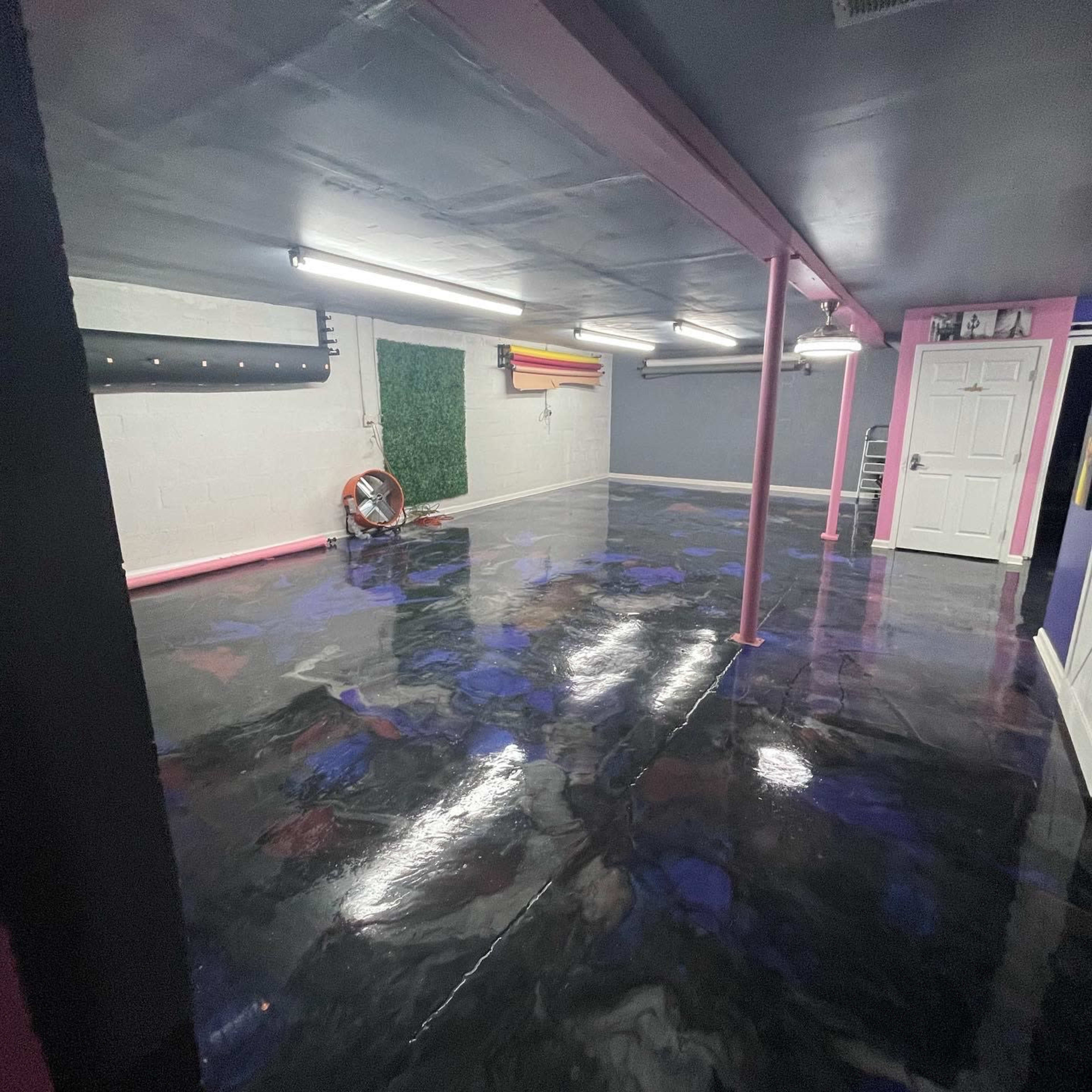 An empty room with a polished black floor, pink support beams, and various wall colors, including a white door and a green wall.