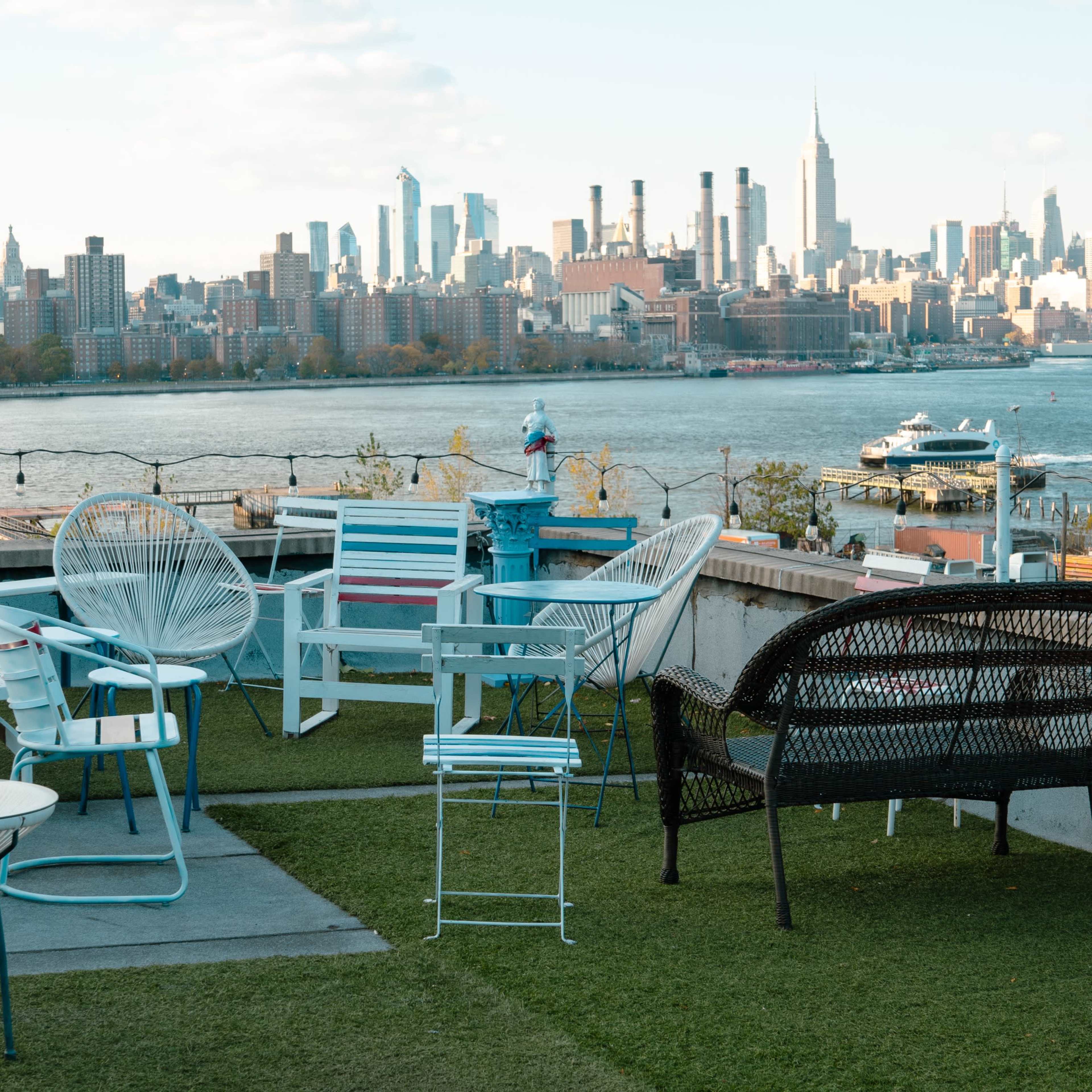 A rooftop terrace with various outdoor chairs and a view of a skyline across the water.