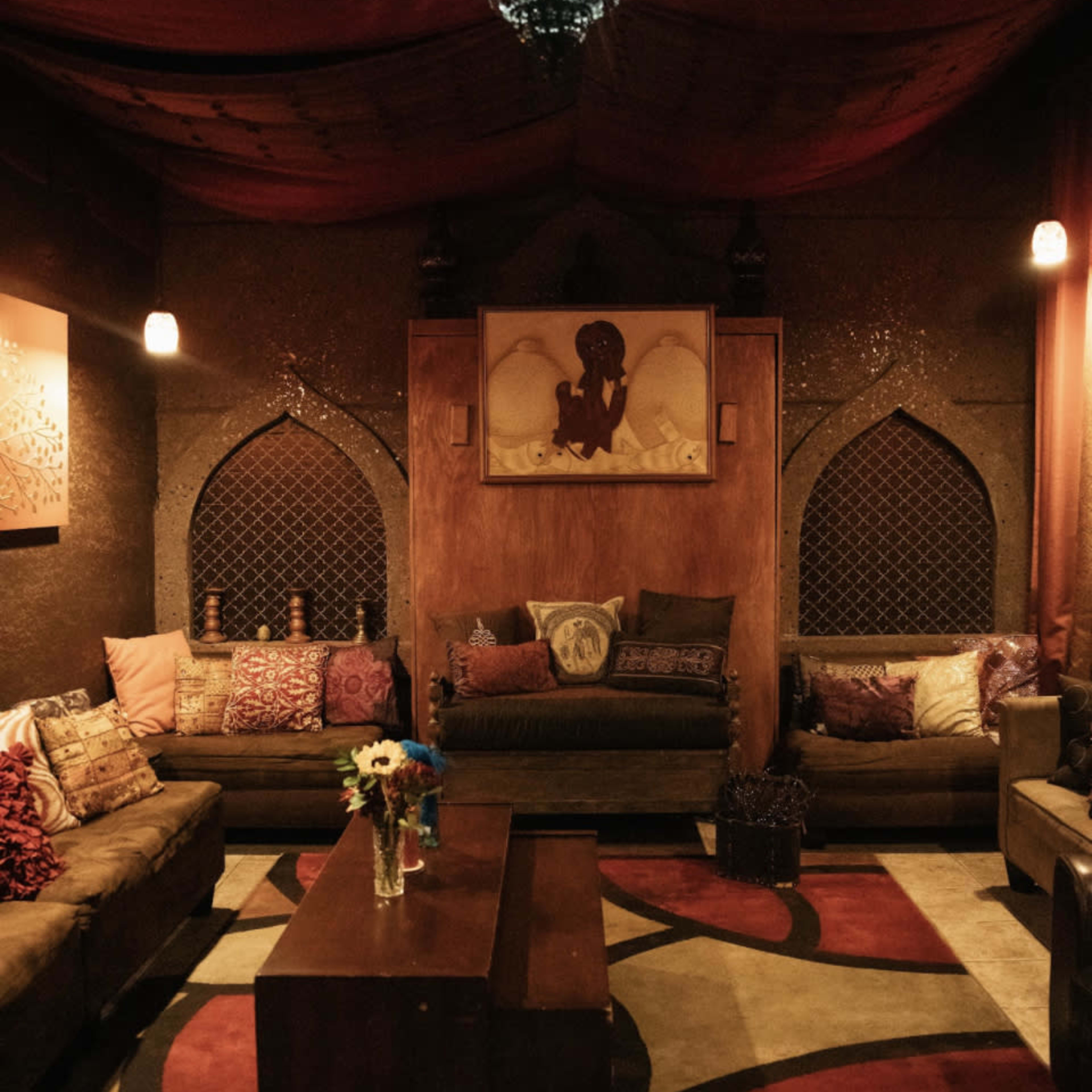 A cozy lounge area with low seating, decorative pillows, and a central coffee table located under a softly lit ceiling.
