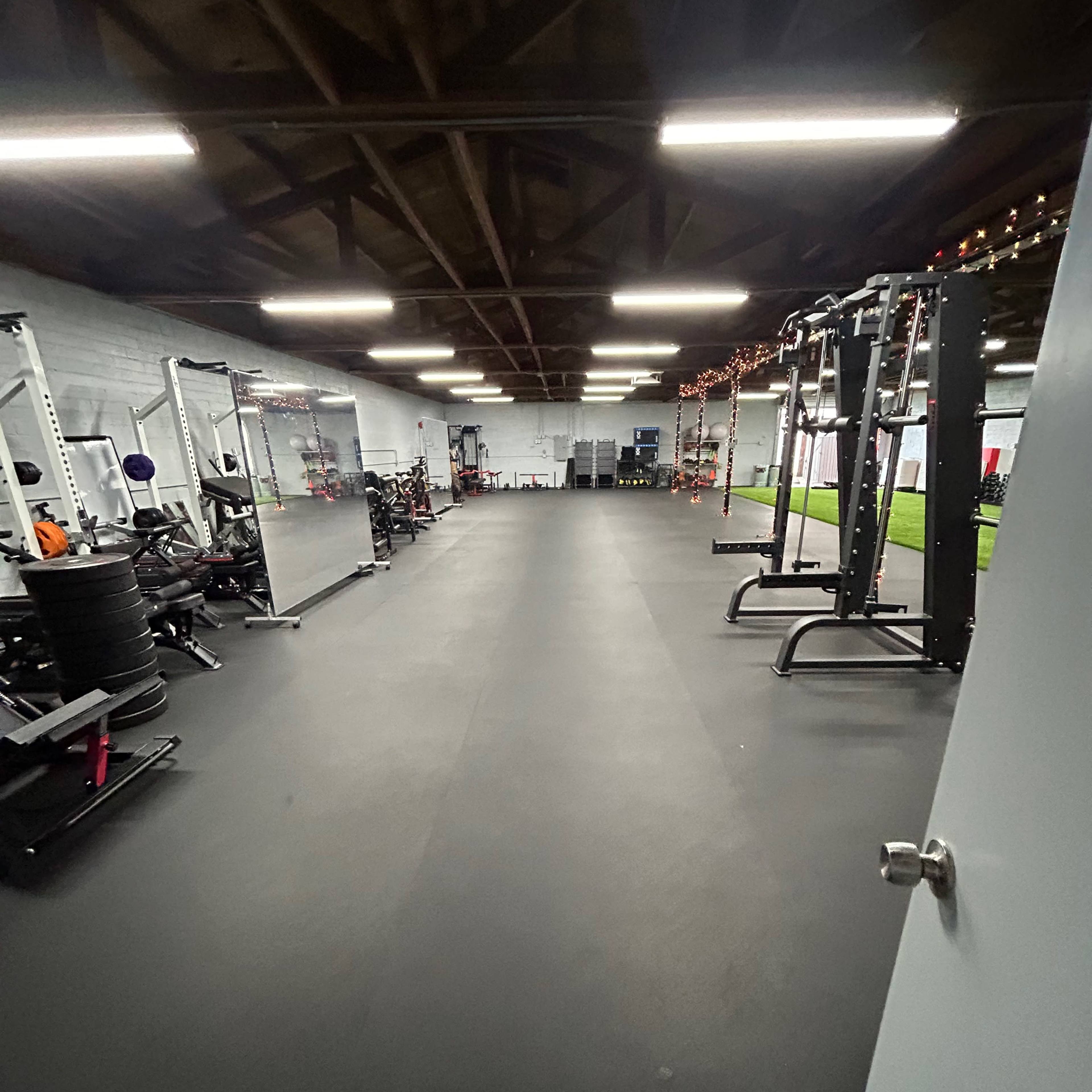 An empty gym interior with various fitness equipment arranged on both sides and a smooth black floor.