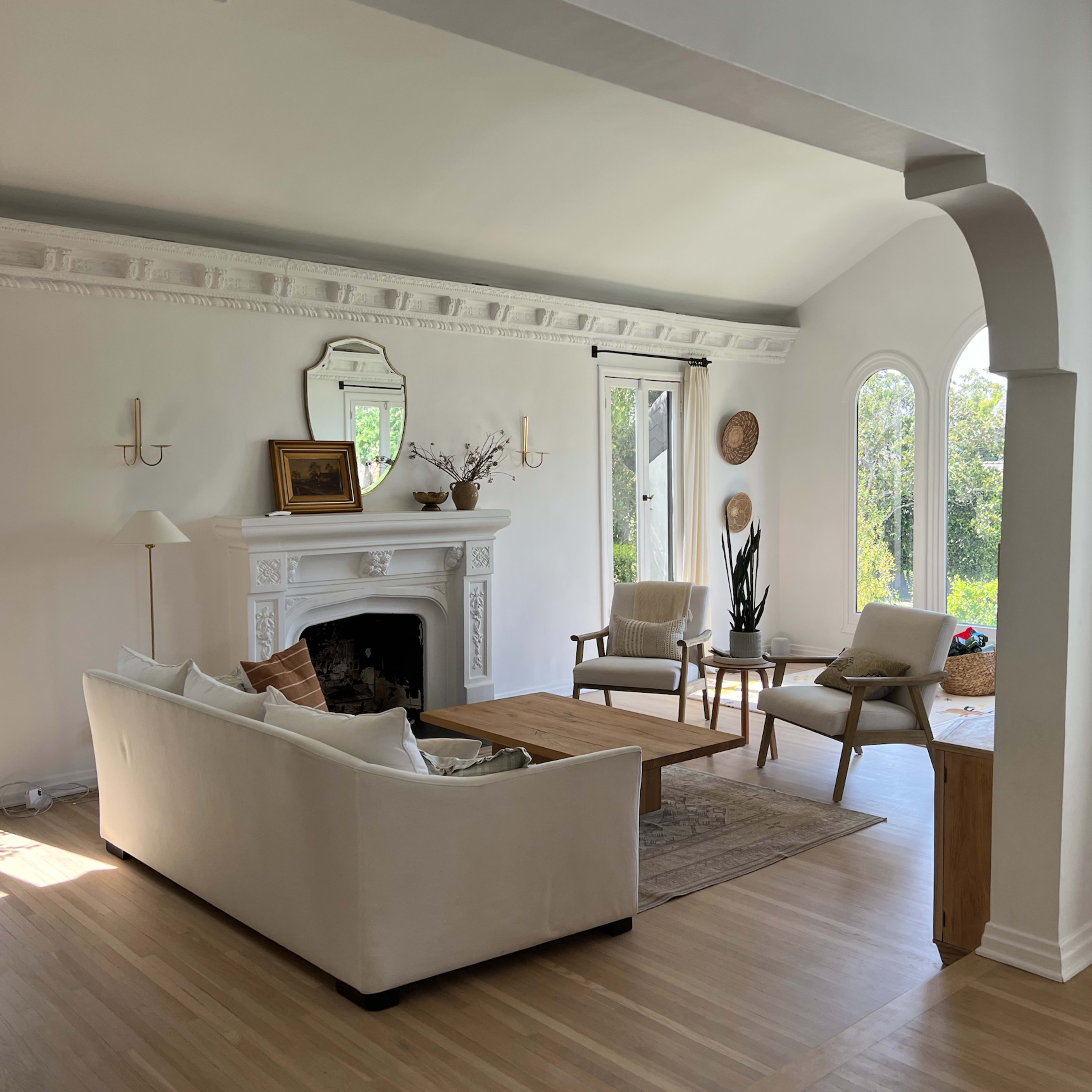 A bright living room with a white sofa, wooden coffee table, and large windows allowing natural light to fill the space.