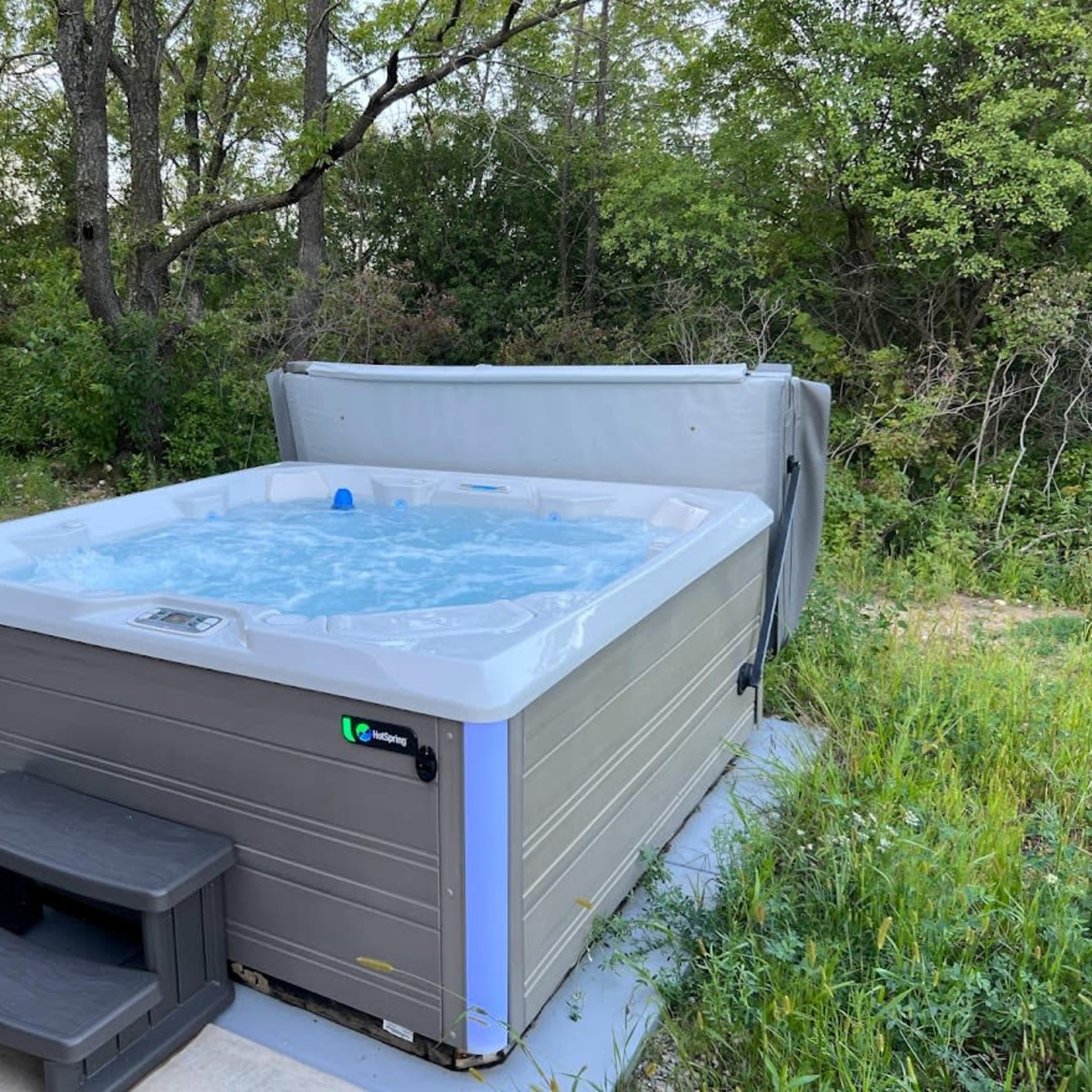 A hot tub sits on a concrete pad surrounded by grass and trees.