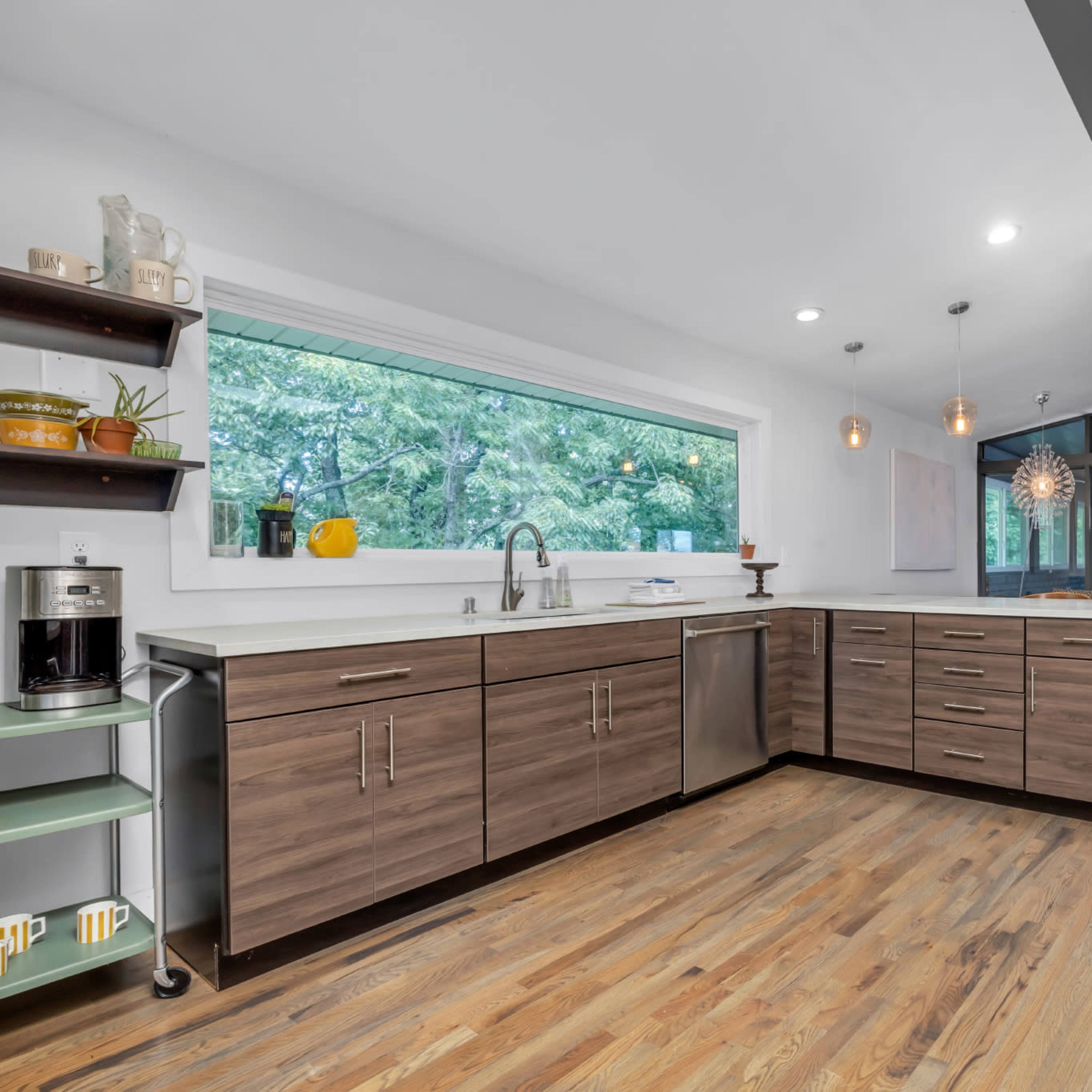 The kitchen features modern cabinetry, a large window overlooking greenery, and hardwood floors.